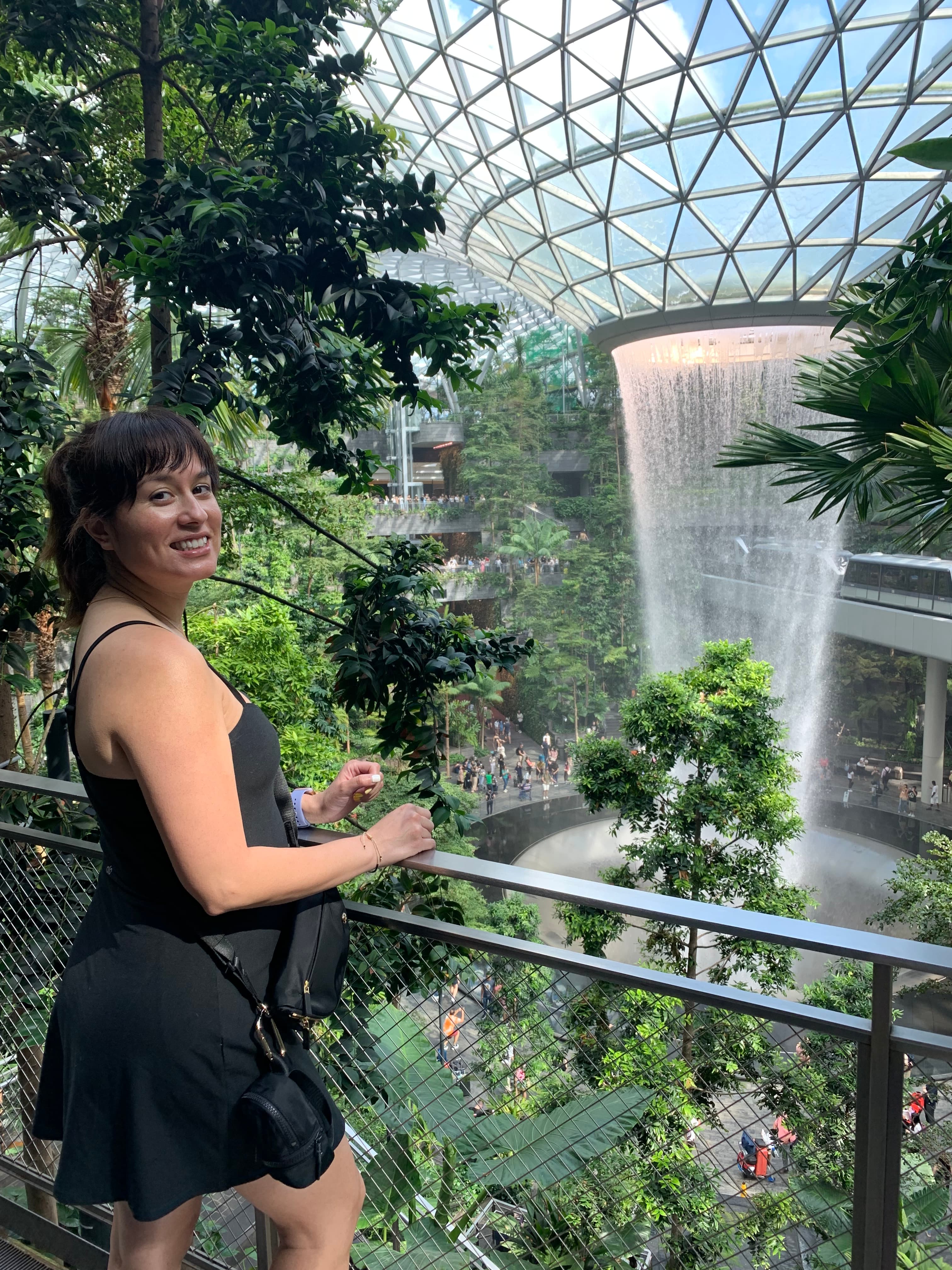 Michelle in a black dress posing in front of the circular indoor waterfall at Singapore airport