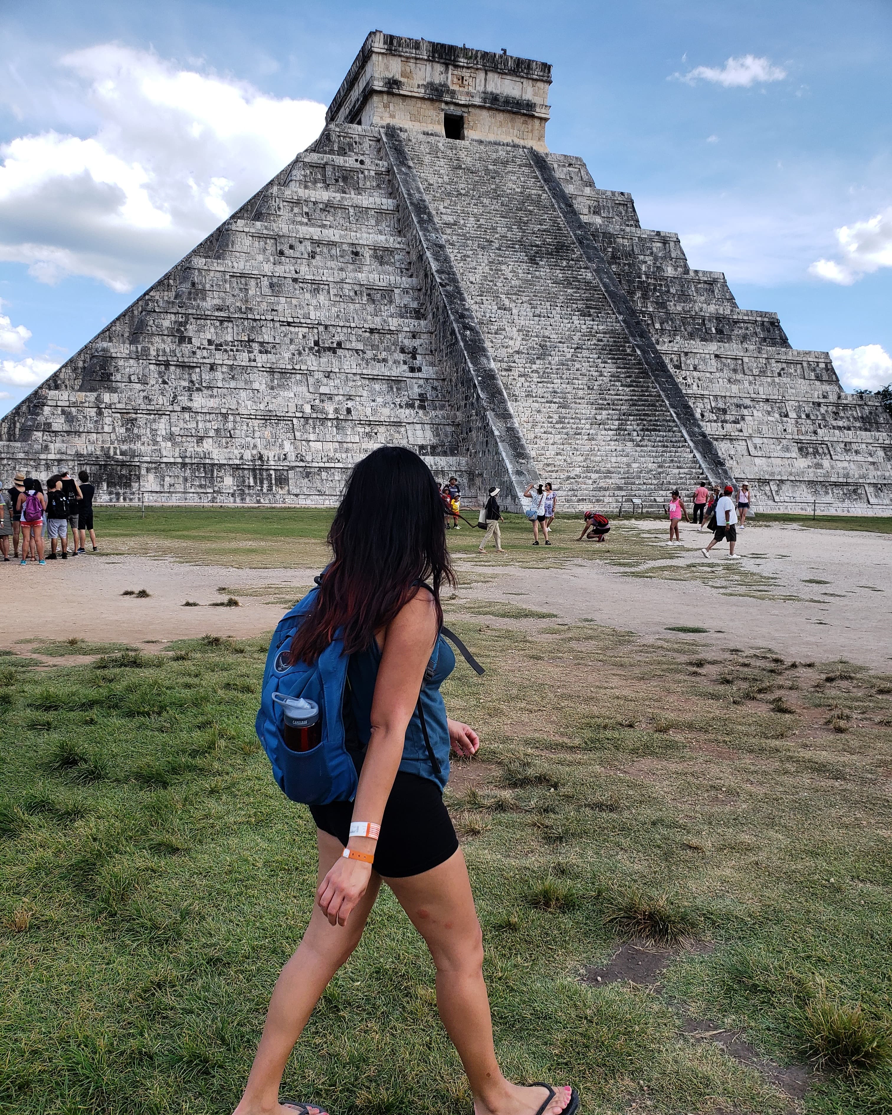 Image of Michelle with a blue backpack walking in front of an ancient pyramid on a sunny day