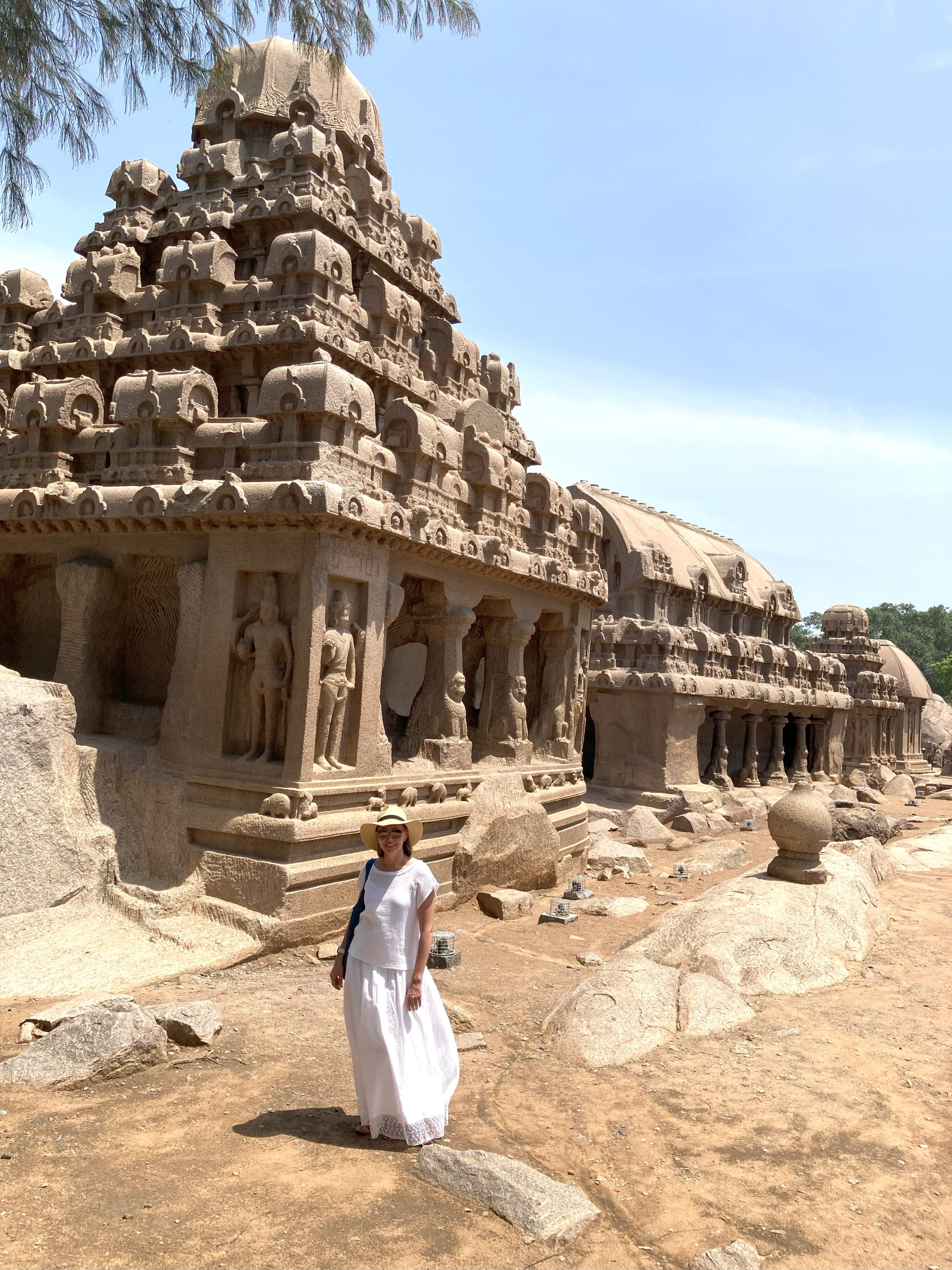 A person in a white gown standing in front of ancient ruins.