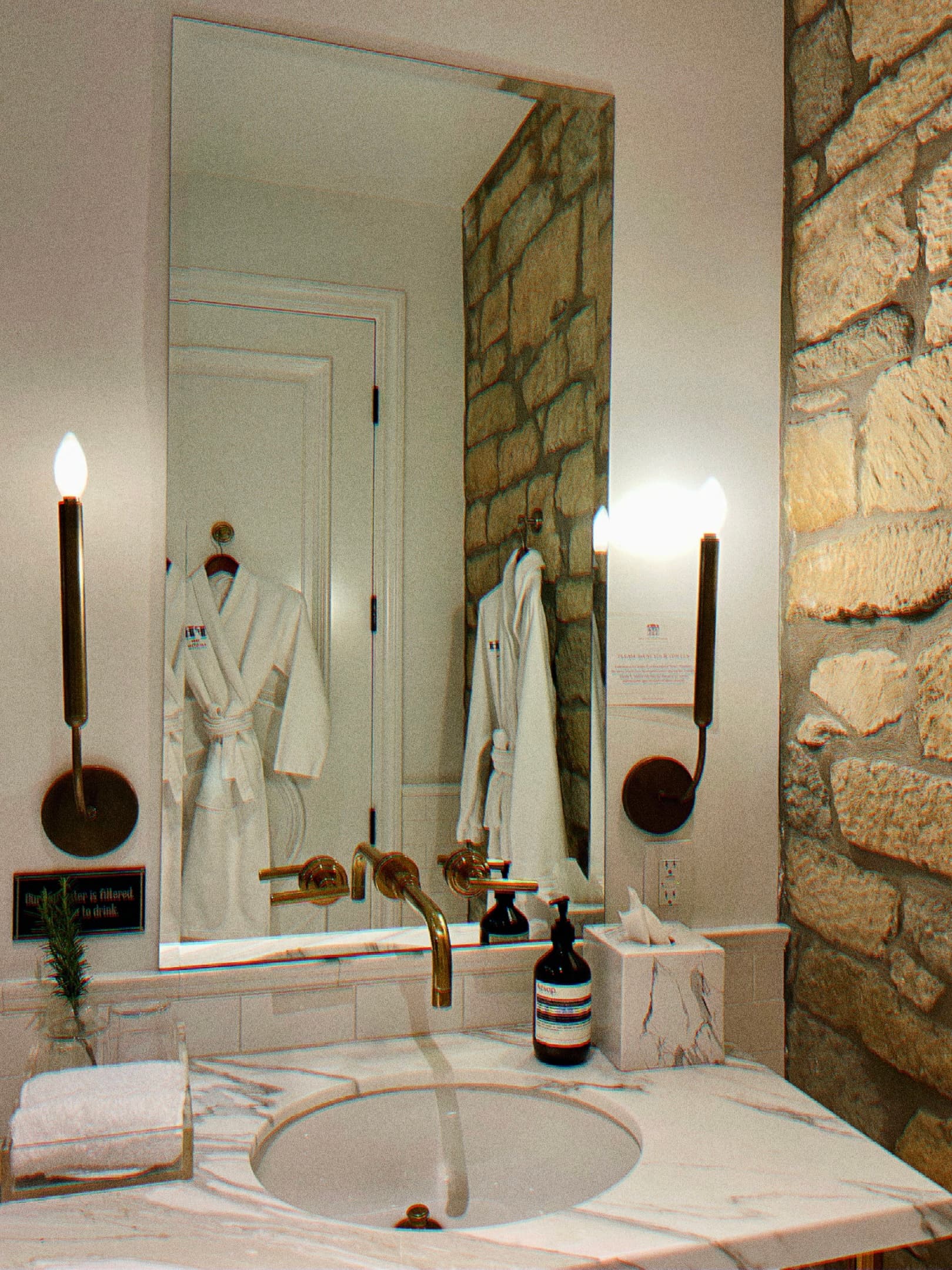 View of a marble sink with bath products and a mirror reflecting two white bathrobes