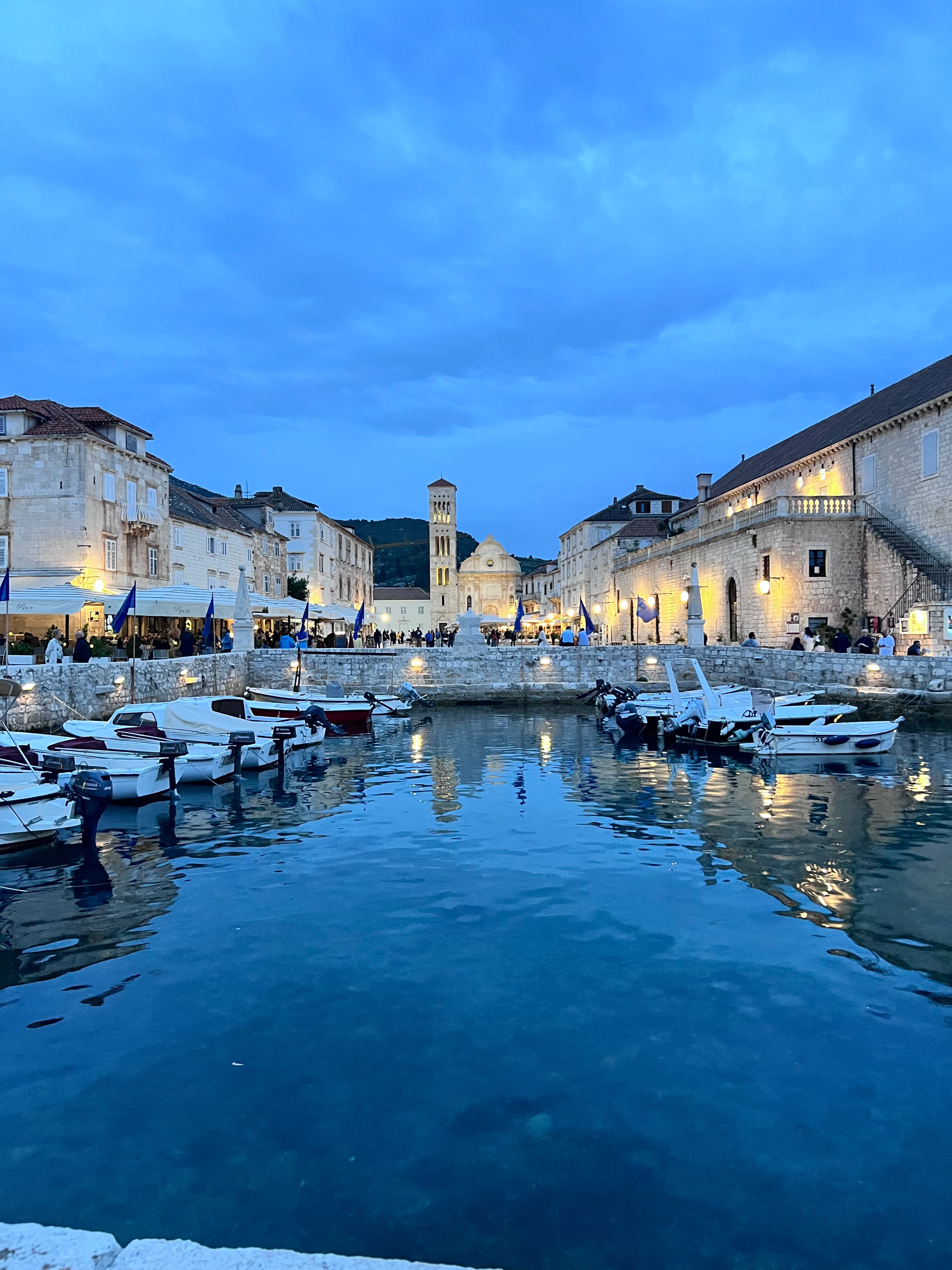 View of a small marina at dusk with small white boats docked and white stone buildings lining the shore