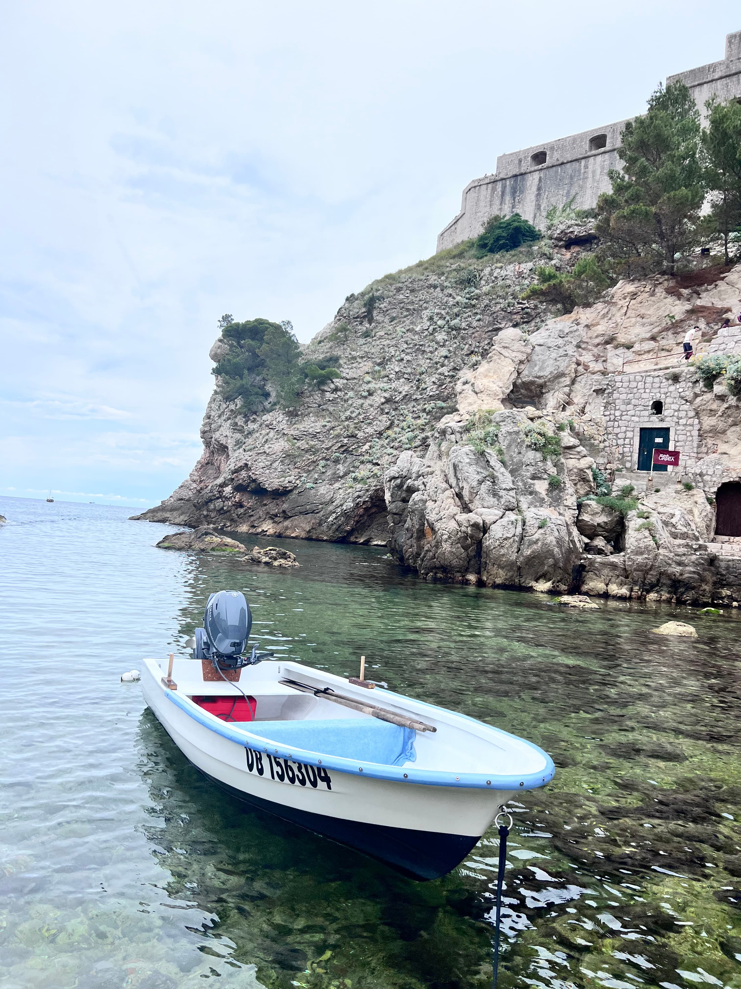 Small white boat floating in shallow water with rocky cliffs behind it
