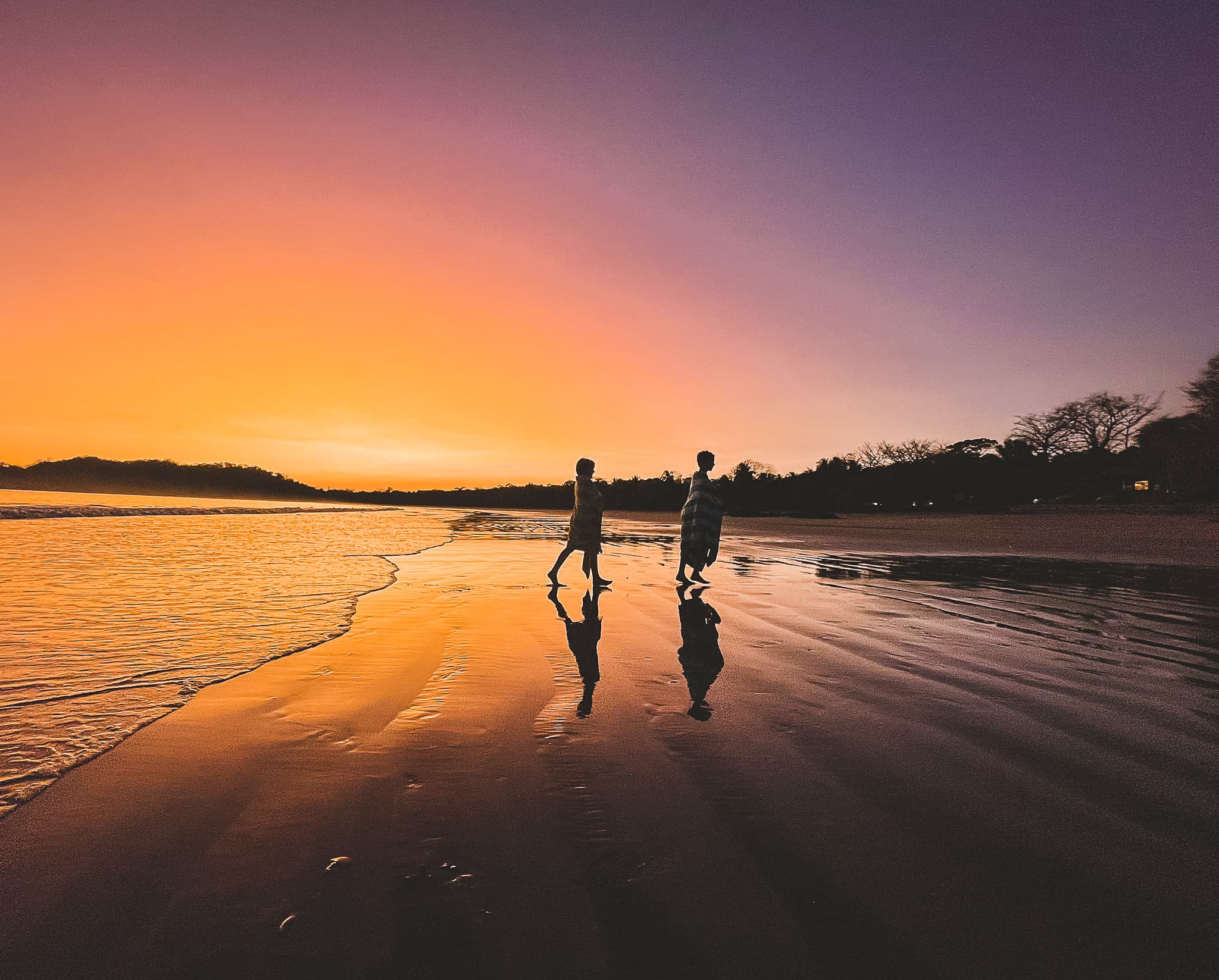 A couple walking on the beach during sunset.
