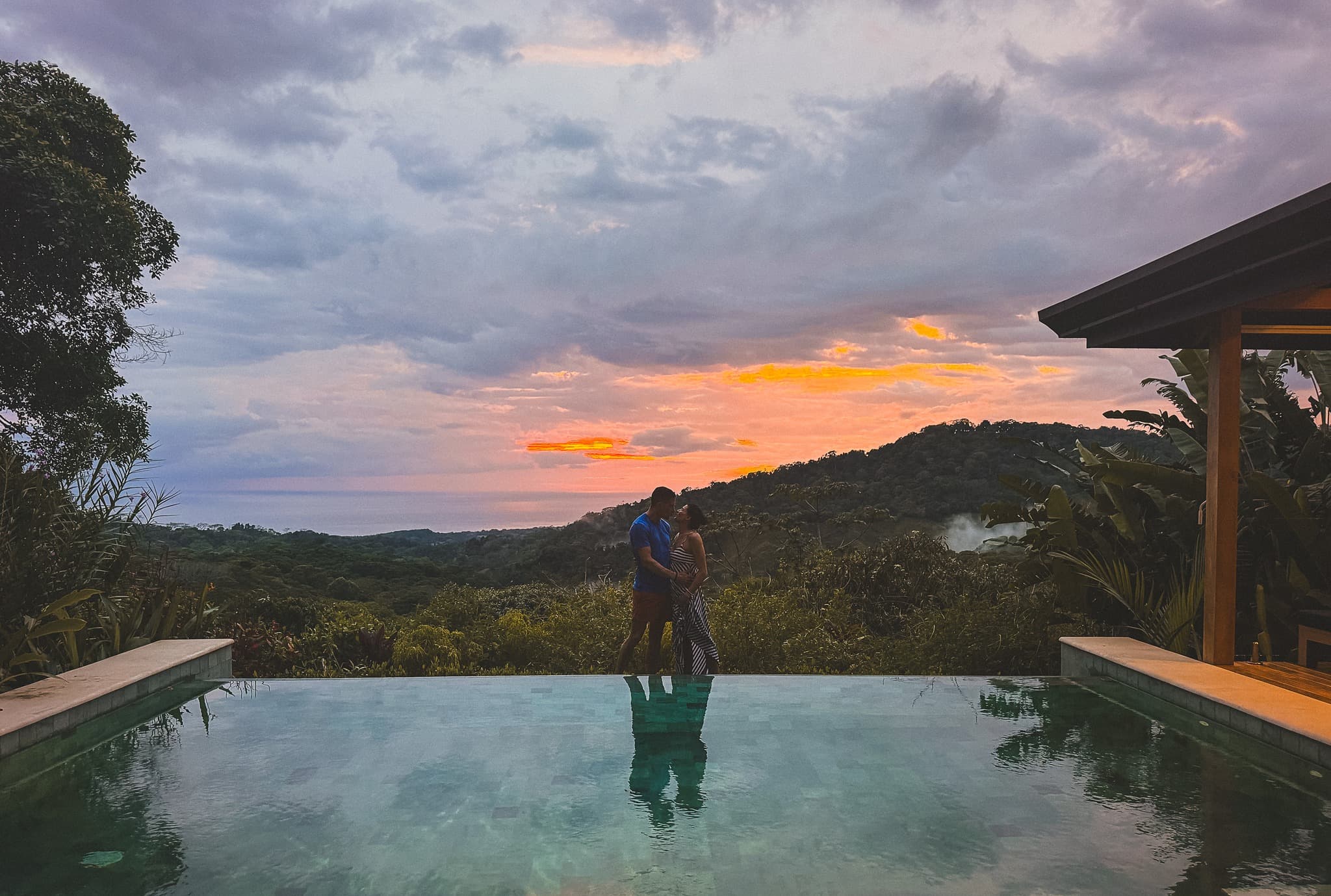 A couple standing at the edge of an infinity pool during sunset.