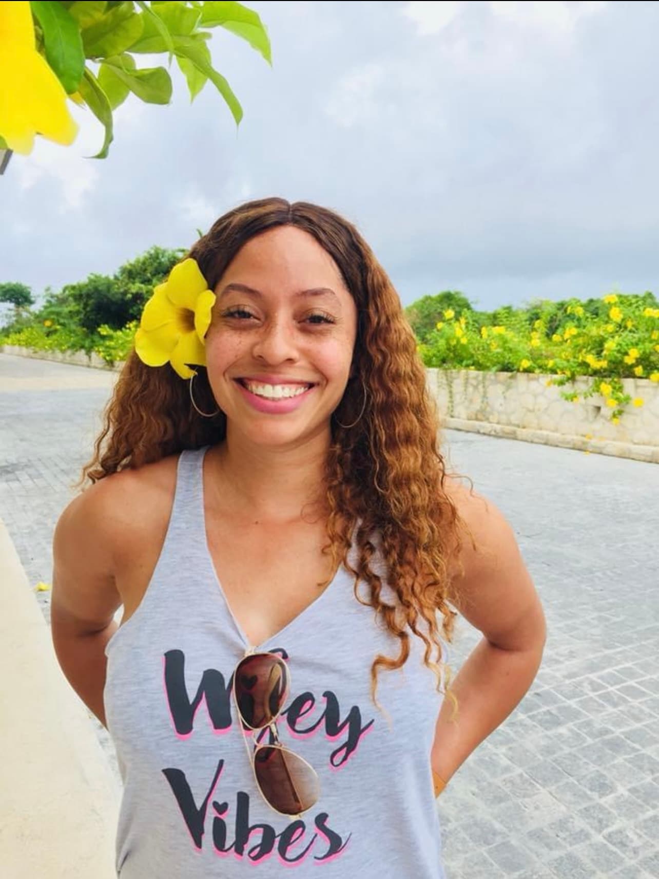 Maria with a yellow flower in her hair smiling for a photo outdoors on a cloudy day