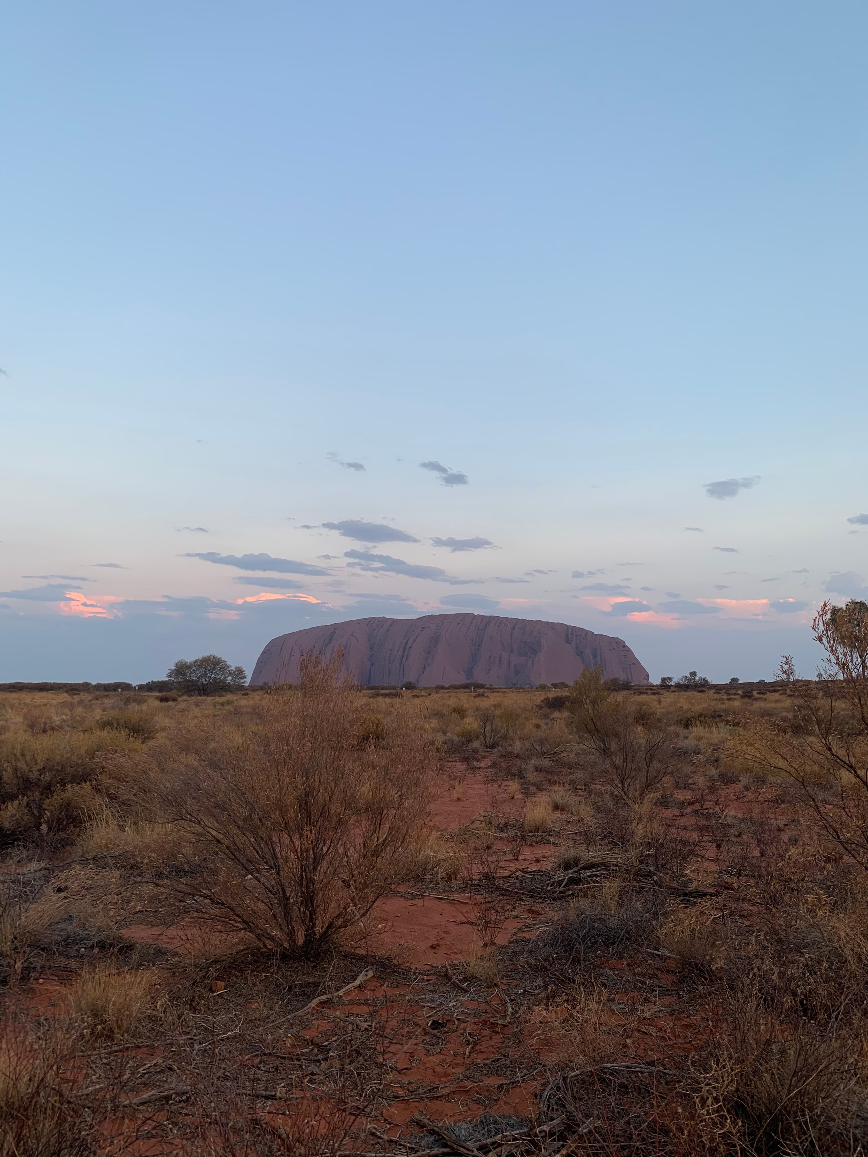 A view of a desert setting at dusk with a rock formation in the distance.