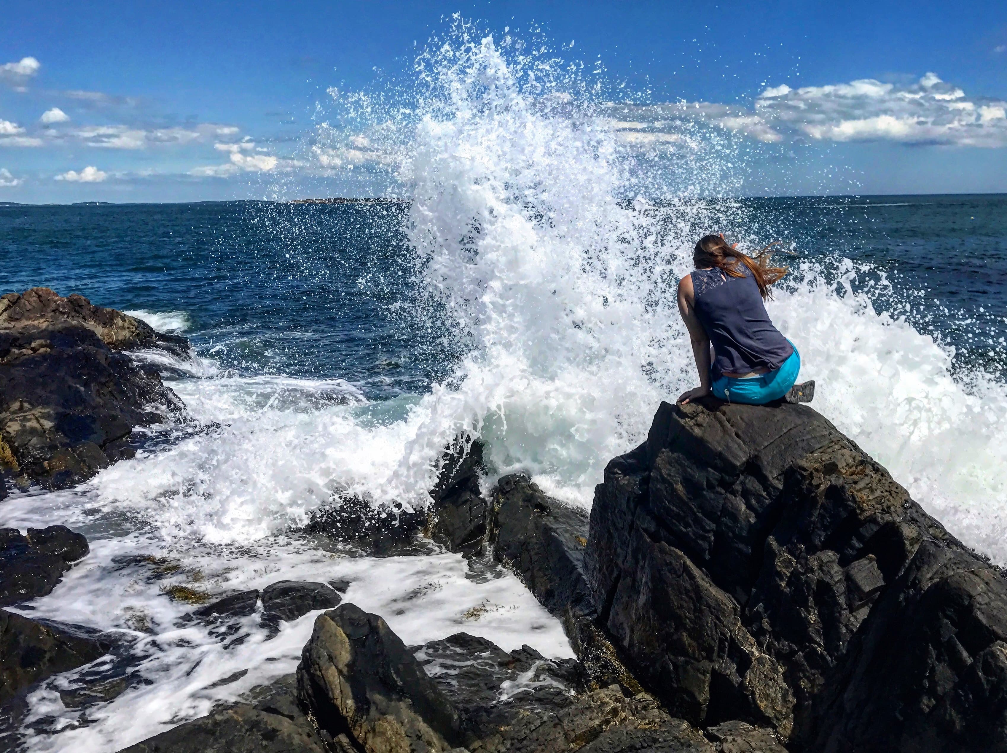 Advisor sitting on a rock in the ocean with waves splashing in the distance.