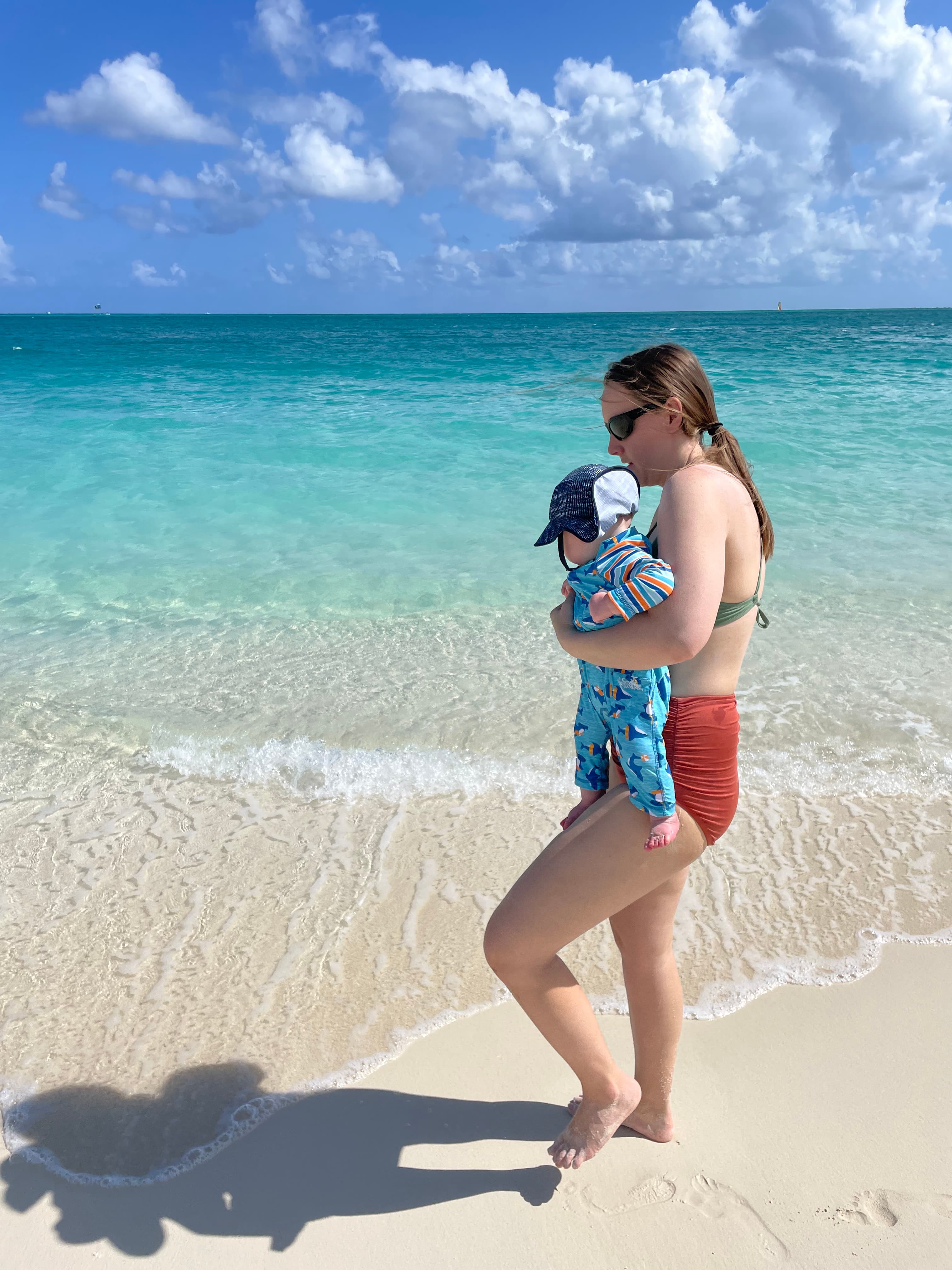 Advisor posing on the beach with her baby on a sunny day with the ocean in the distance.