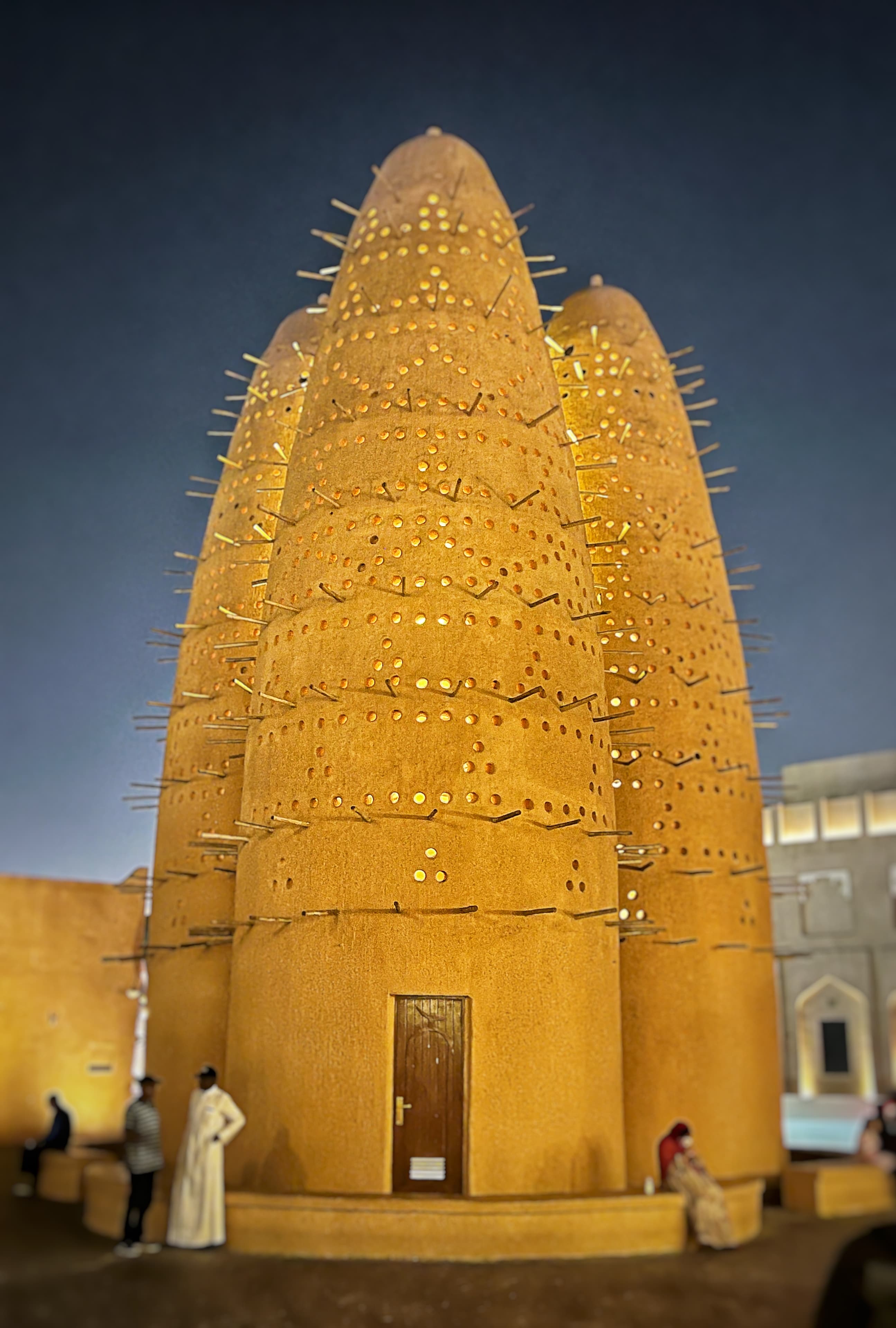 View of a few people standing by a cone-shaped structure with a small door at night