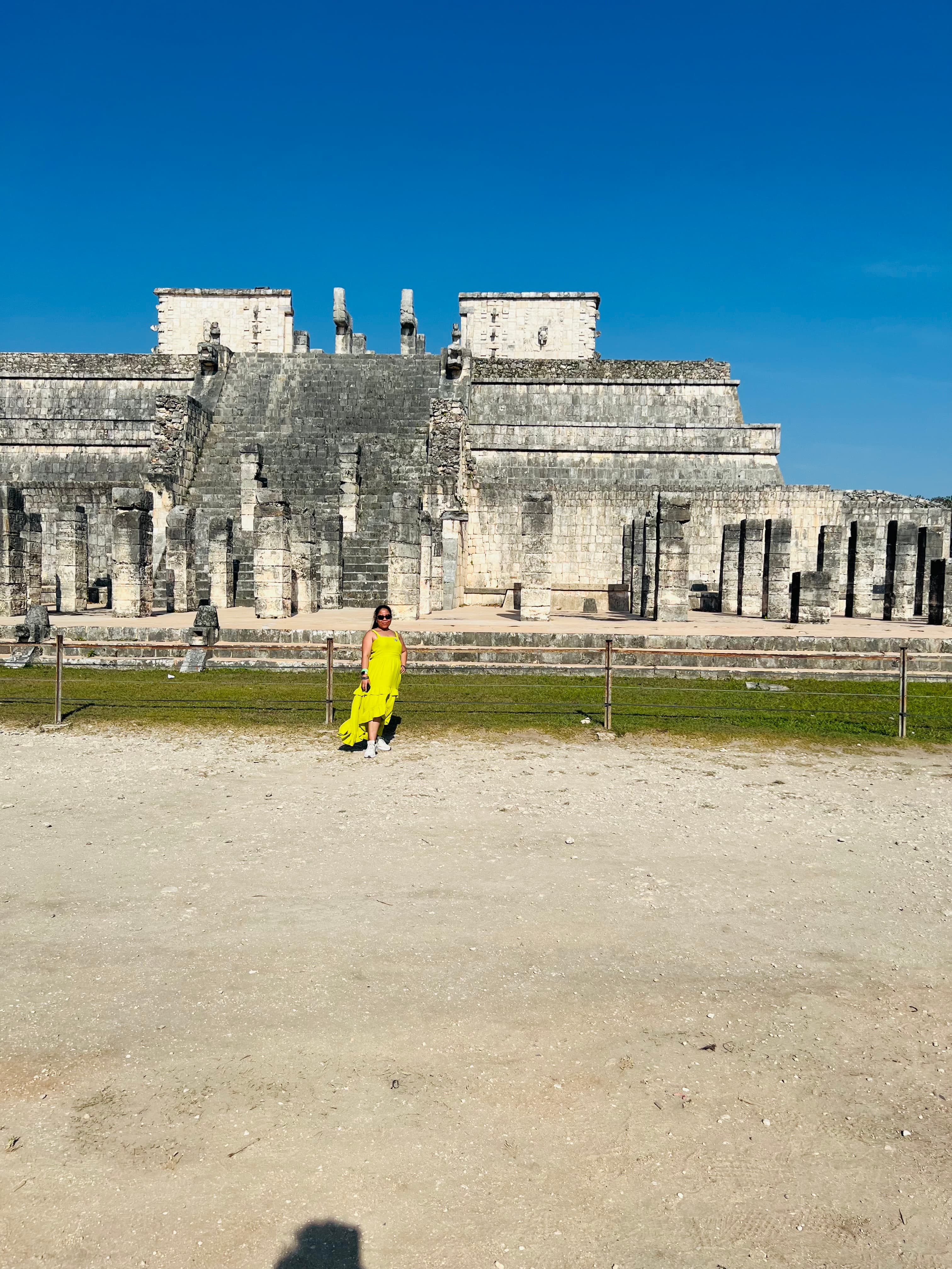 Image of Rogelyn in a yellow dress in front of an old building on a sunny day