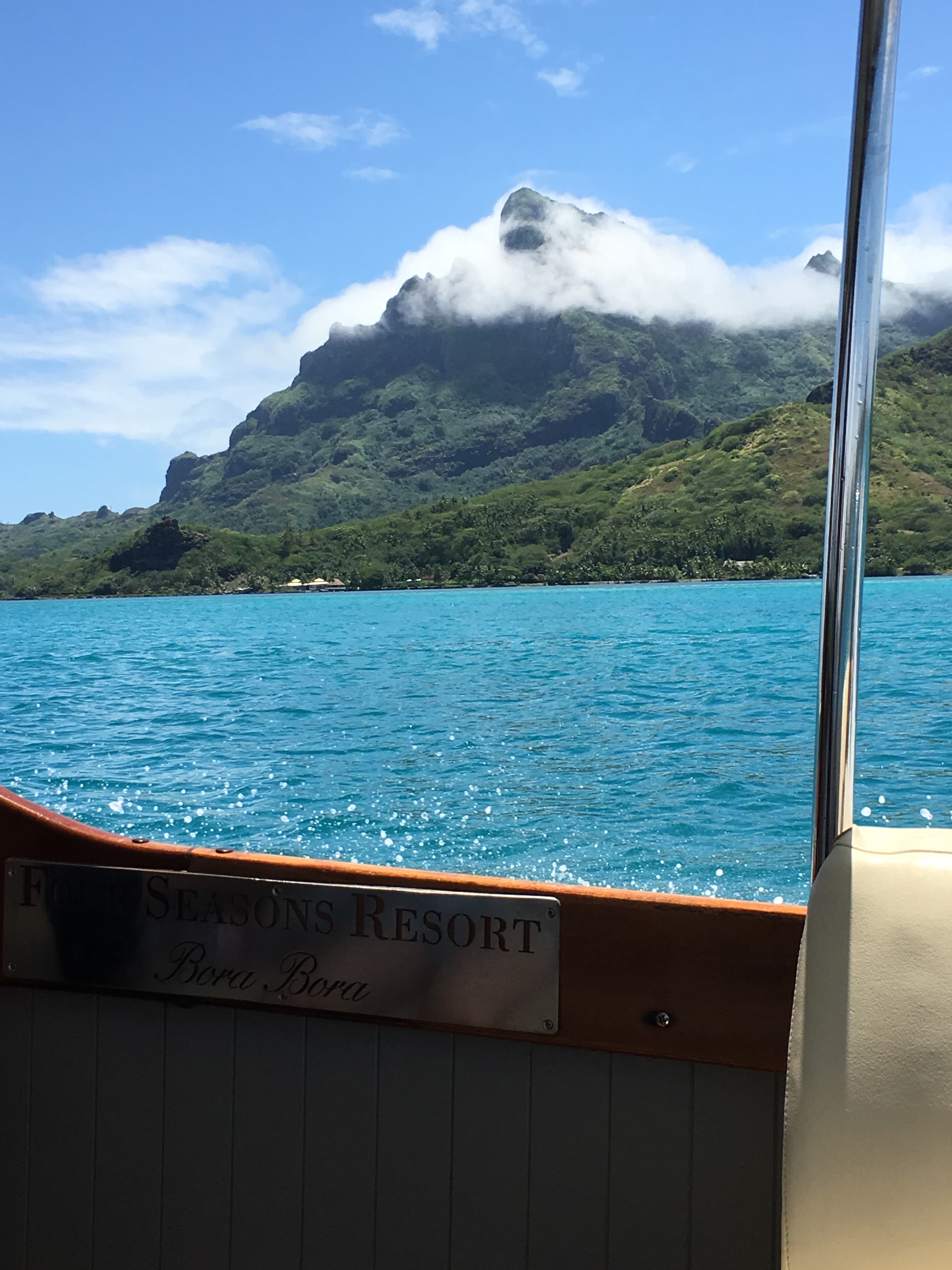 Pretty view from a boat of a bright blue sea with lush green mountains surrounded by clouds in the distance