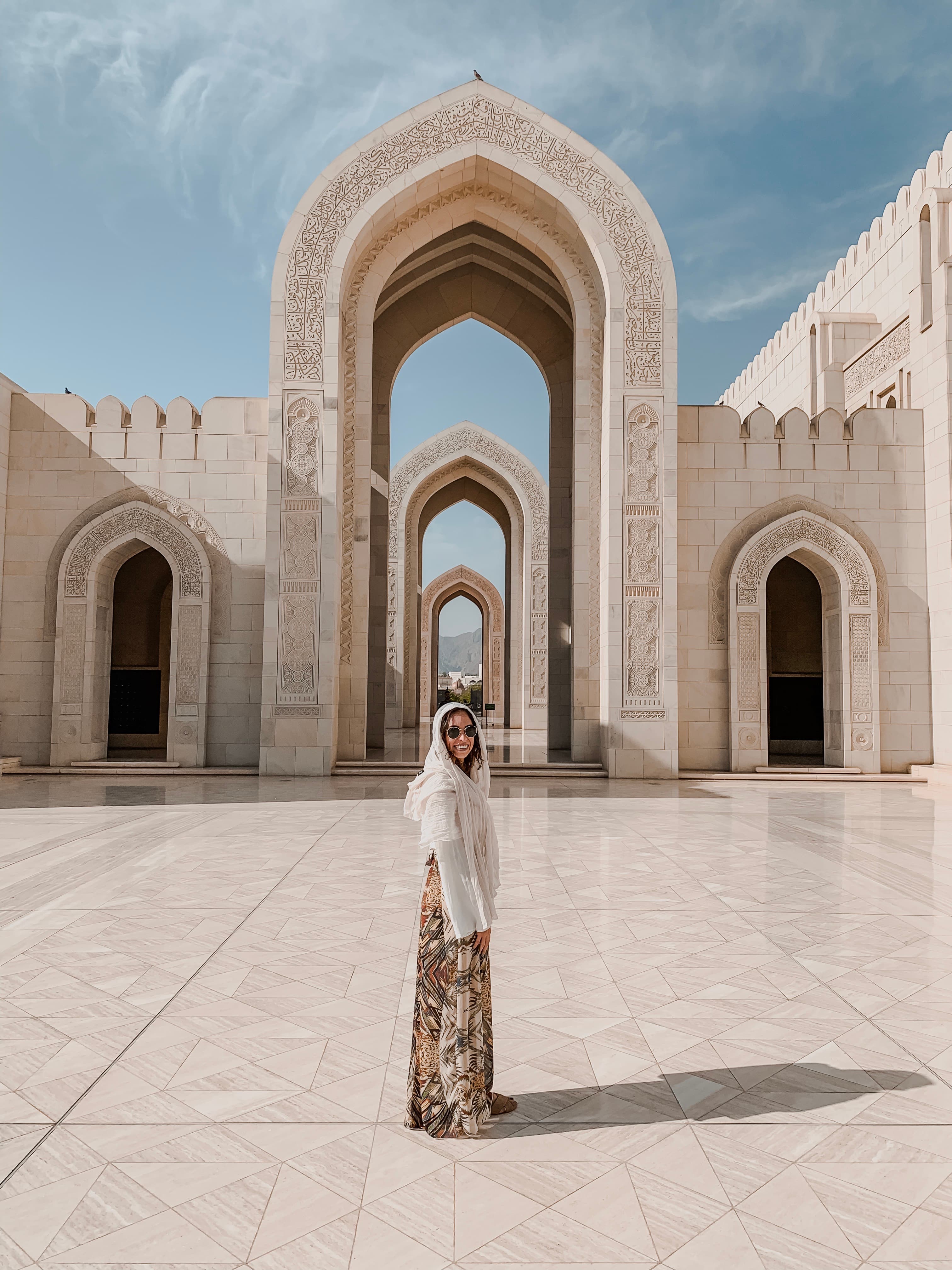 Janine in a white shirt and shawl in front of a white marble mosque on a sunny day