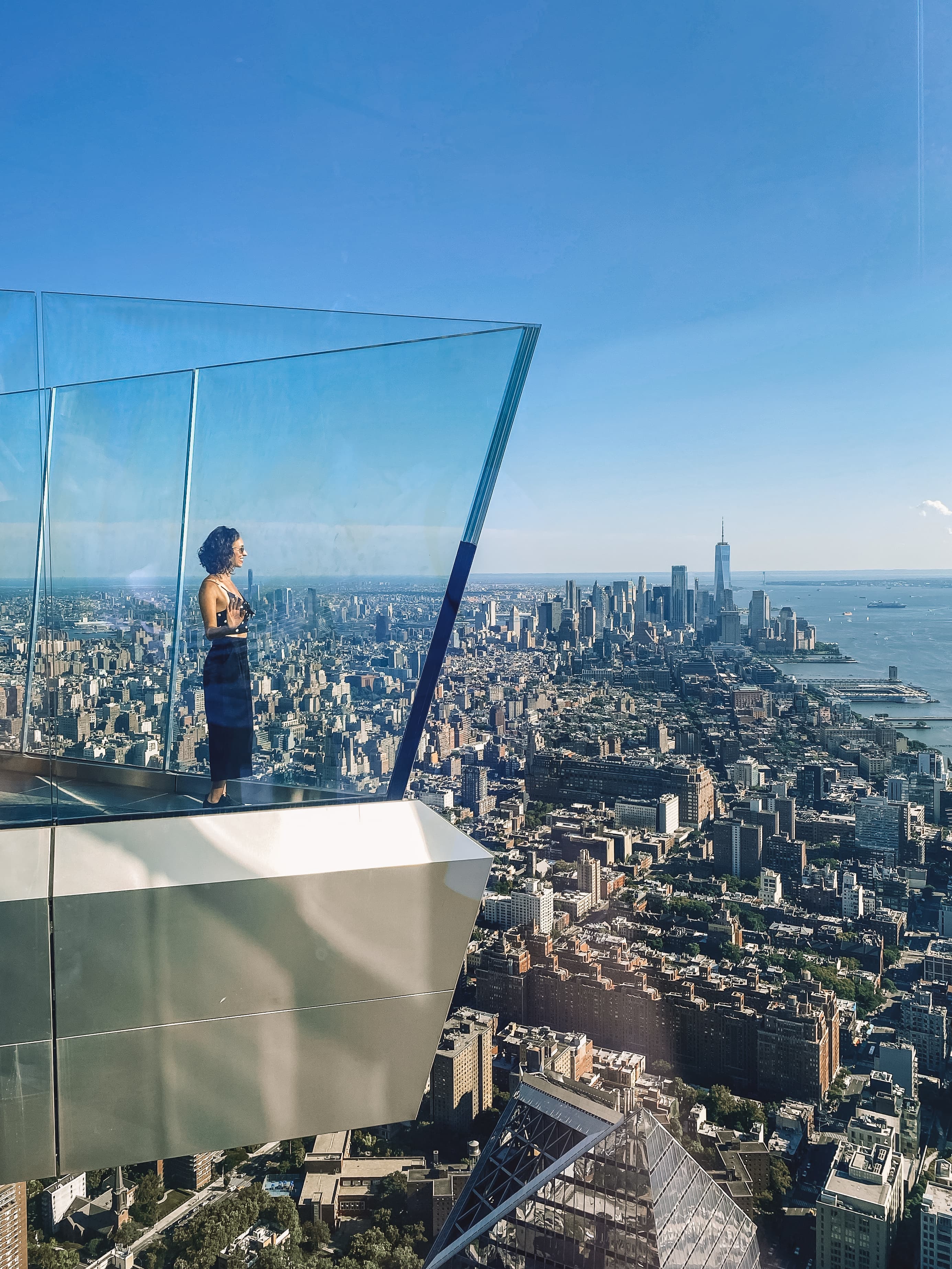 Janine in a black outfit standing at a lookout point with clear views of Manhattan in the distance