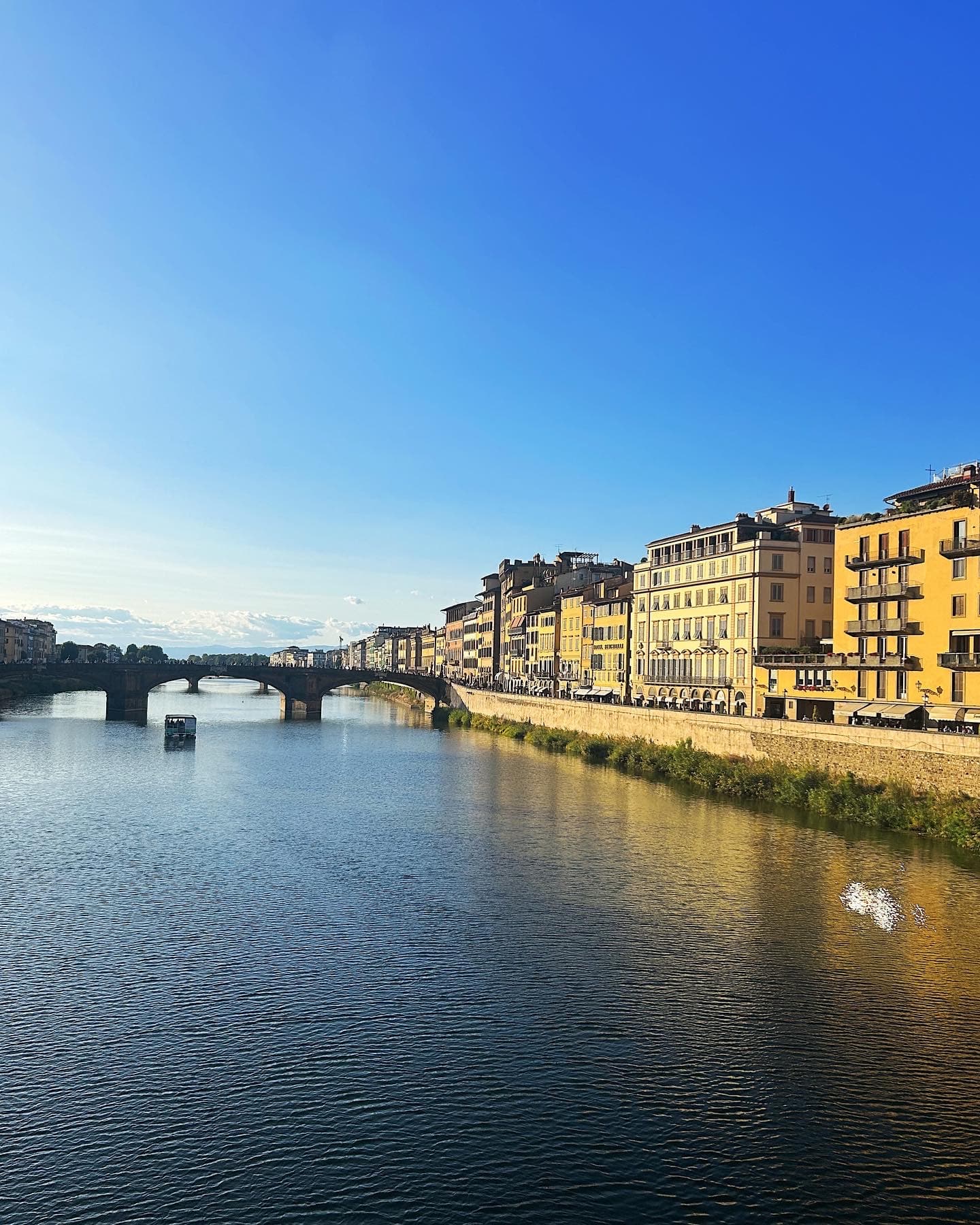 Beautiful view of a wide canal and yellow buildings with an arched bridge in the distance on a clear day