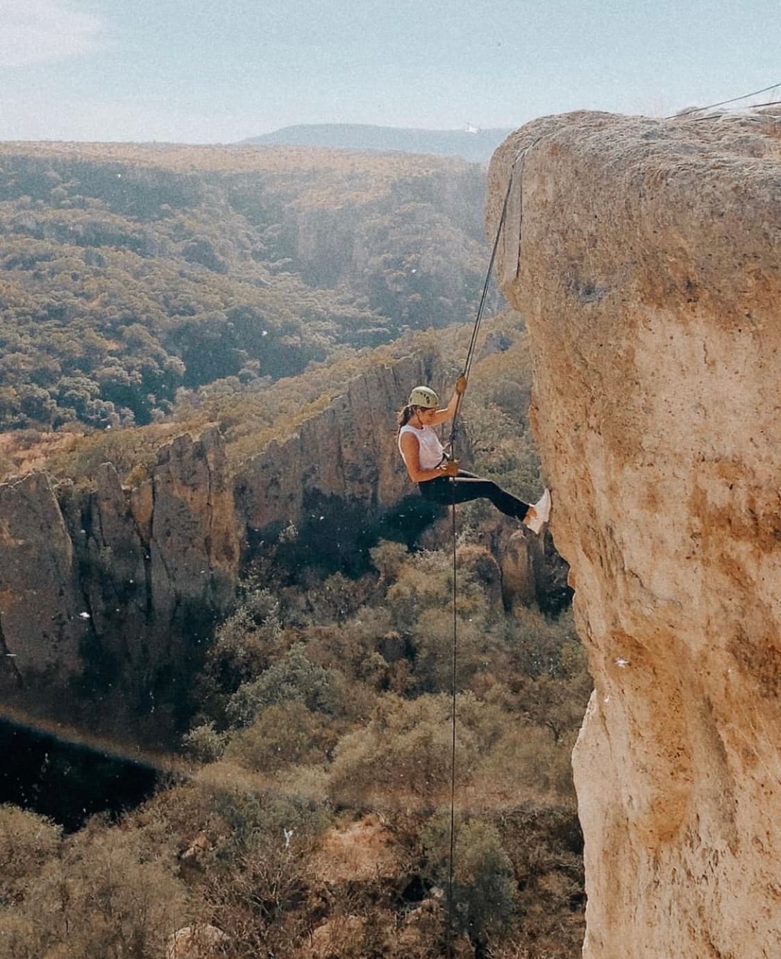Advisor rappelling off a cliff with mountains in the background.