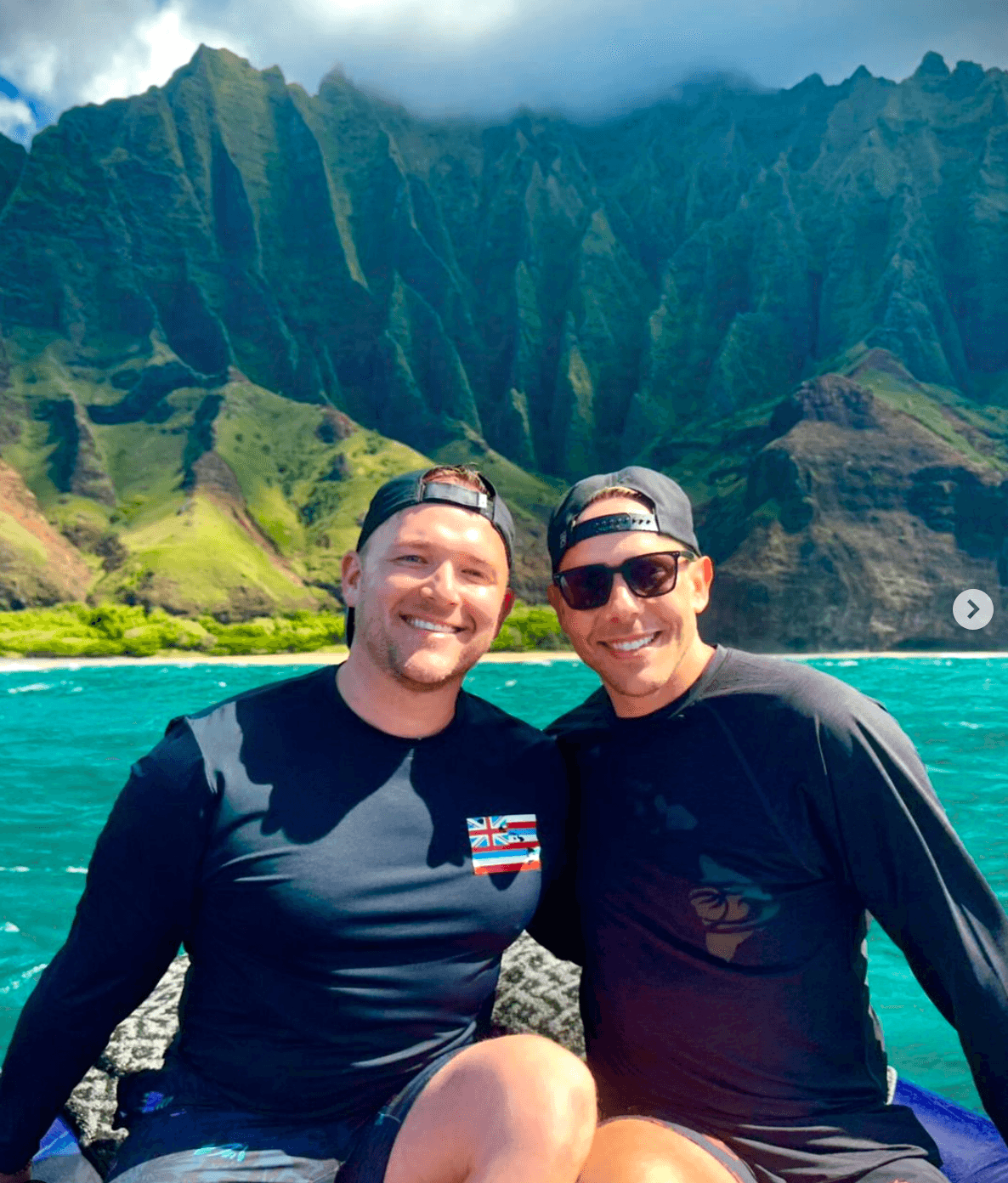 Andrew and a man in backwards baseball caps smiling for a photo on a bright blue lake with beautiful mountain background