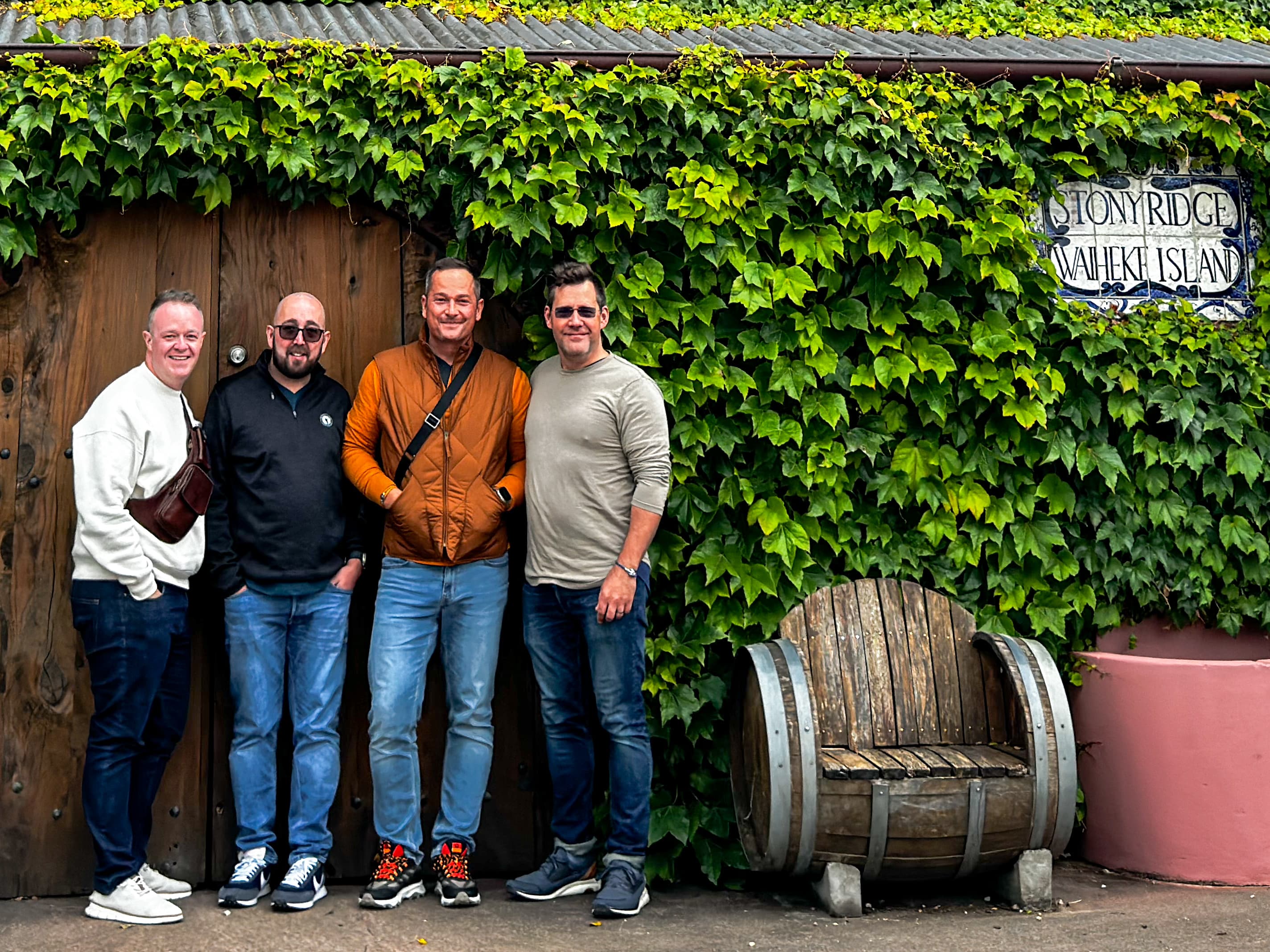 Advisor and three men posing in front of a wall covered in vines