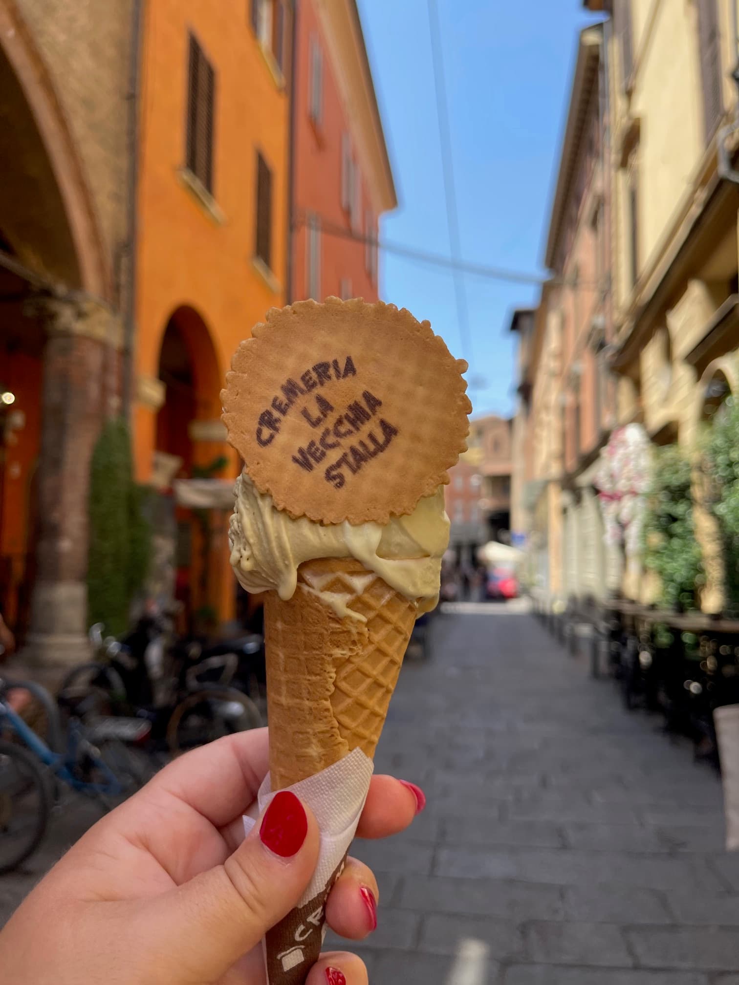 Someone holding a waffle cone with a historical street behind them with yellow and white buildings.