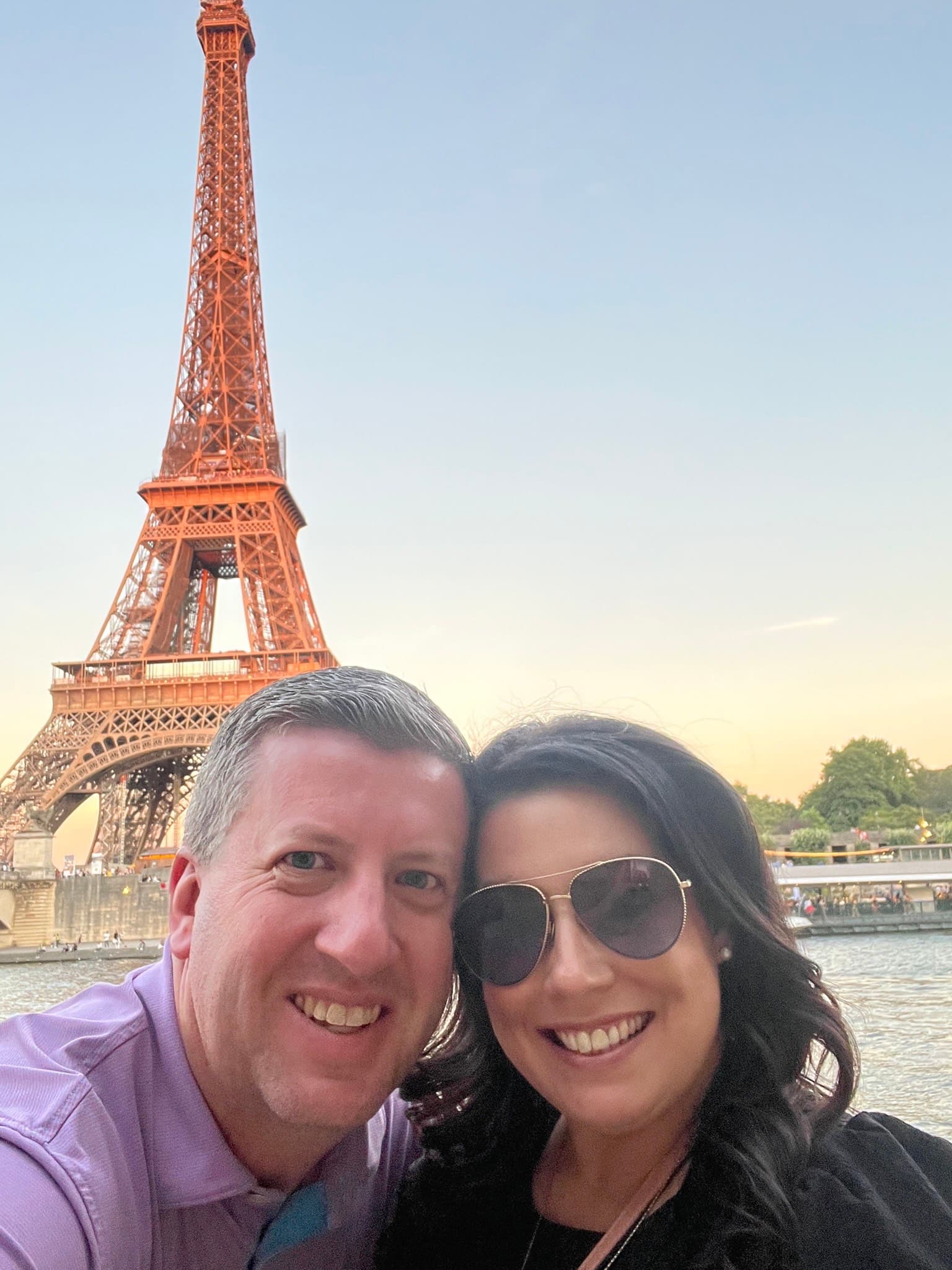 A man and woman smiling in front of the Eiffel Tower at sunset in Paris, France.