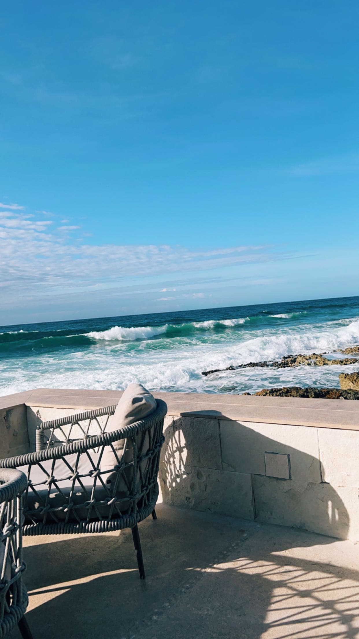 A seating area on an outside balcony with the ocean in the distance on a sunny day.