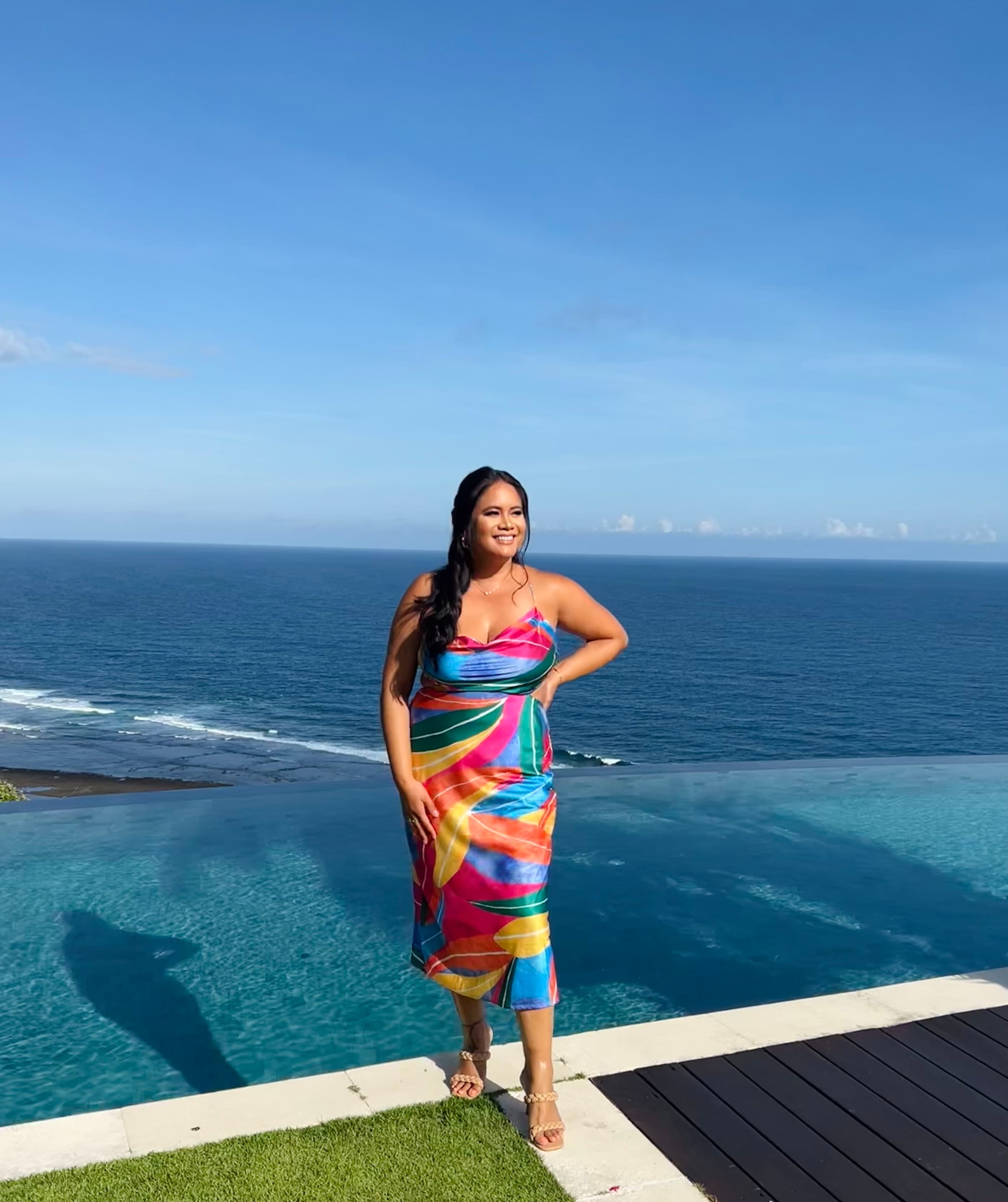 Leah in a colorful dress posing on a balcony overlooking the sea on a sunny day