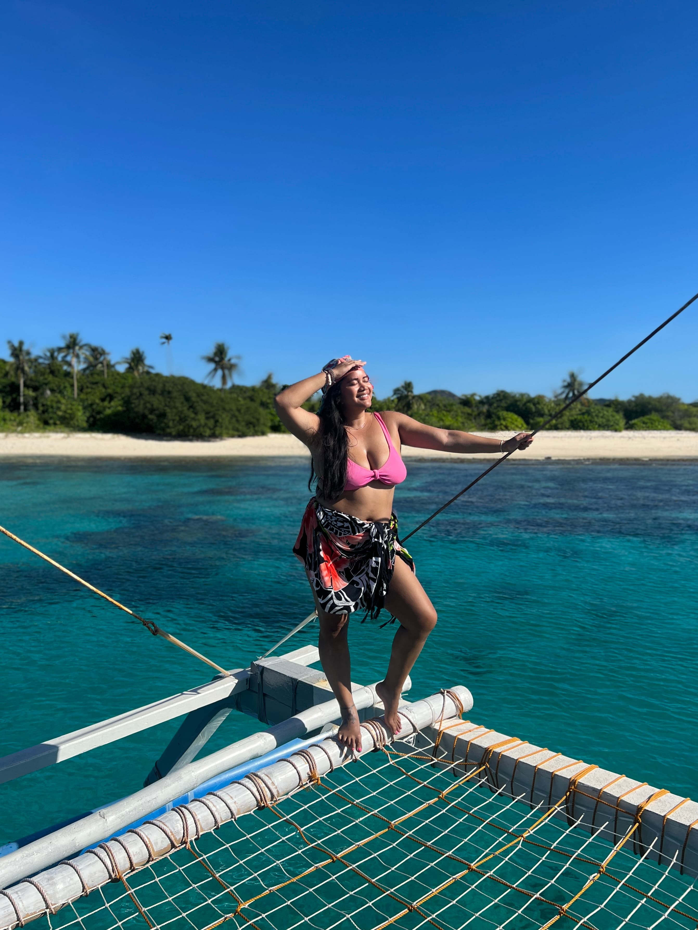 Leah in a pink pathing suit standing on a net hanging over the ocean with a beautiful beach visible behind her