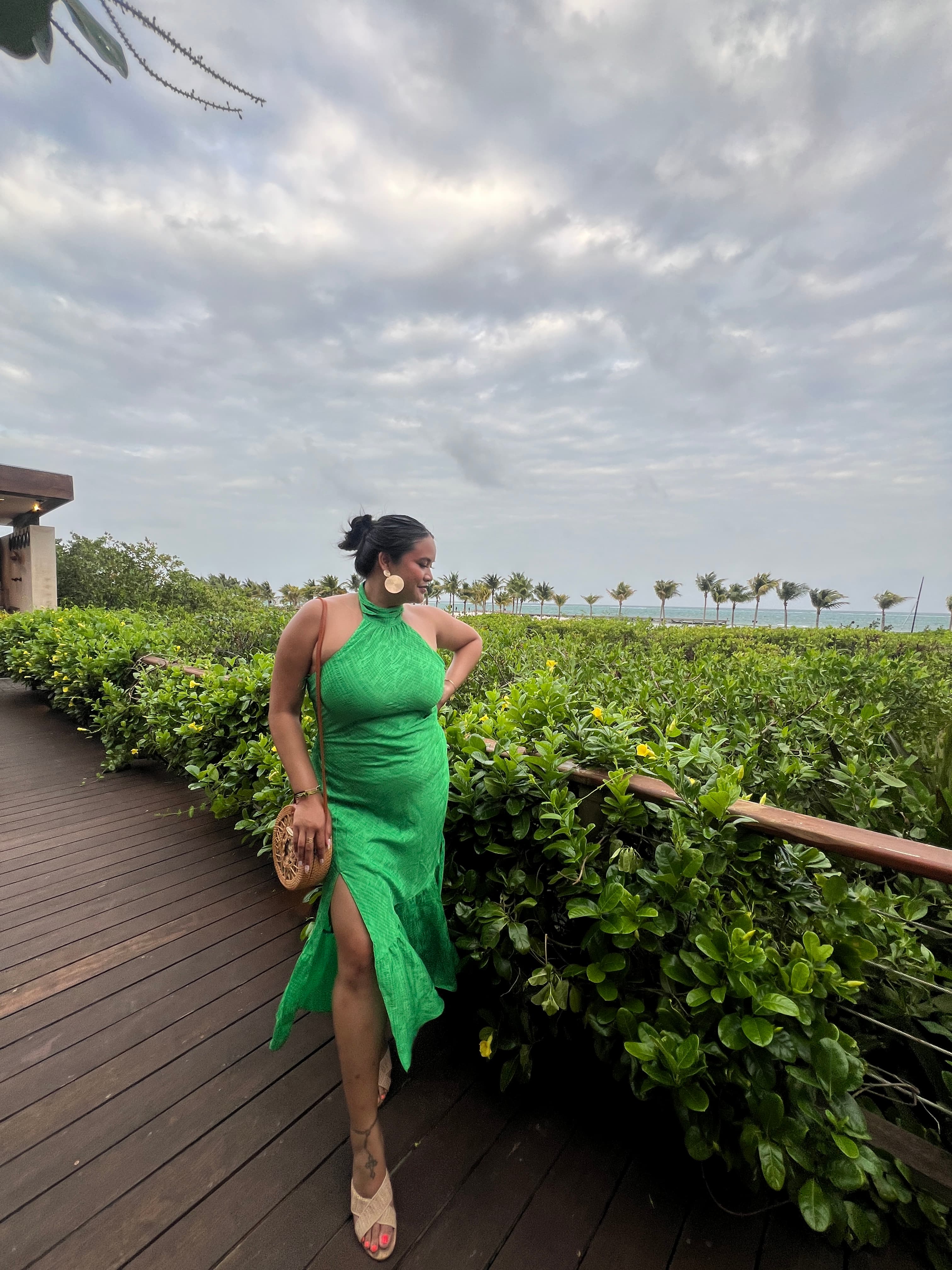 Leah in a green dress and heels looking out over a field of green plants on a cloudy day