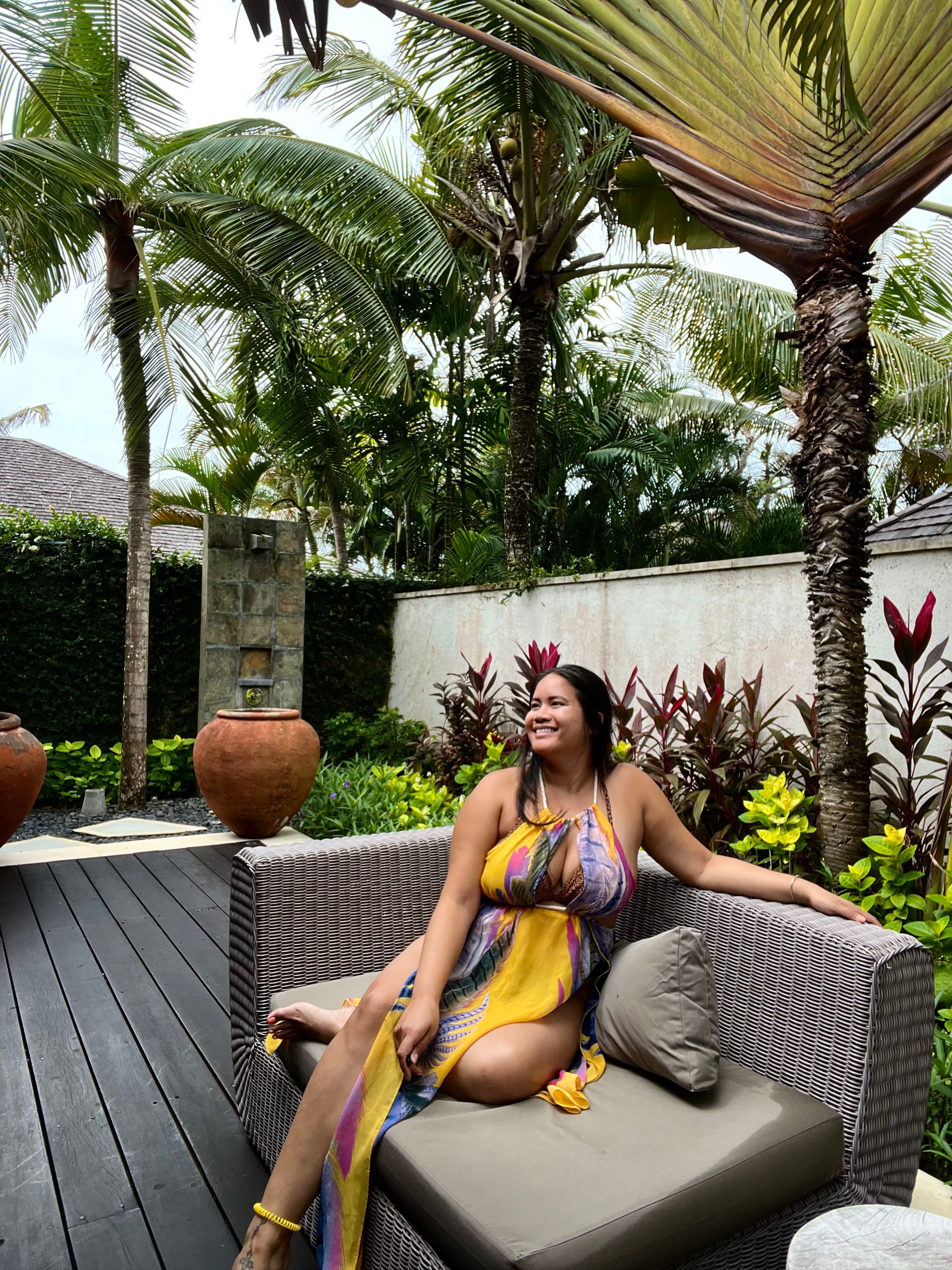 Leah sitting on a grey lounge chair under palm trees and other plants