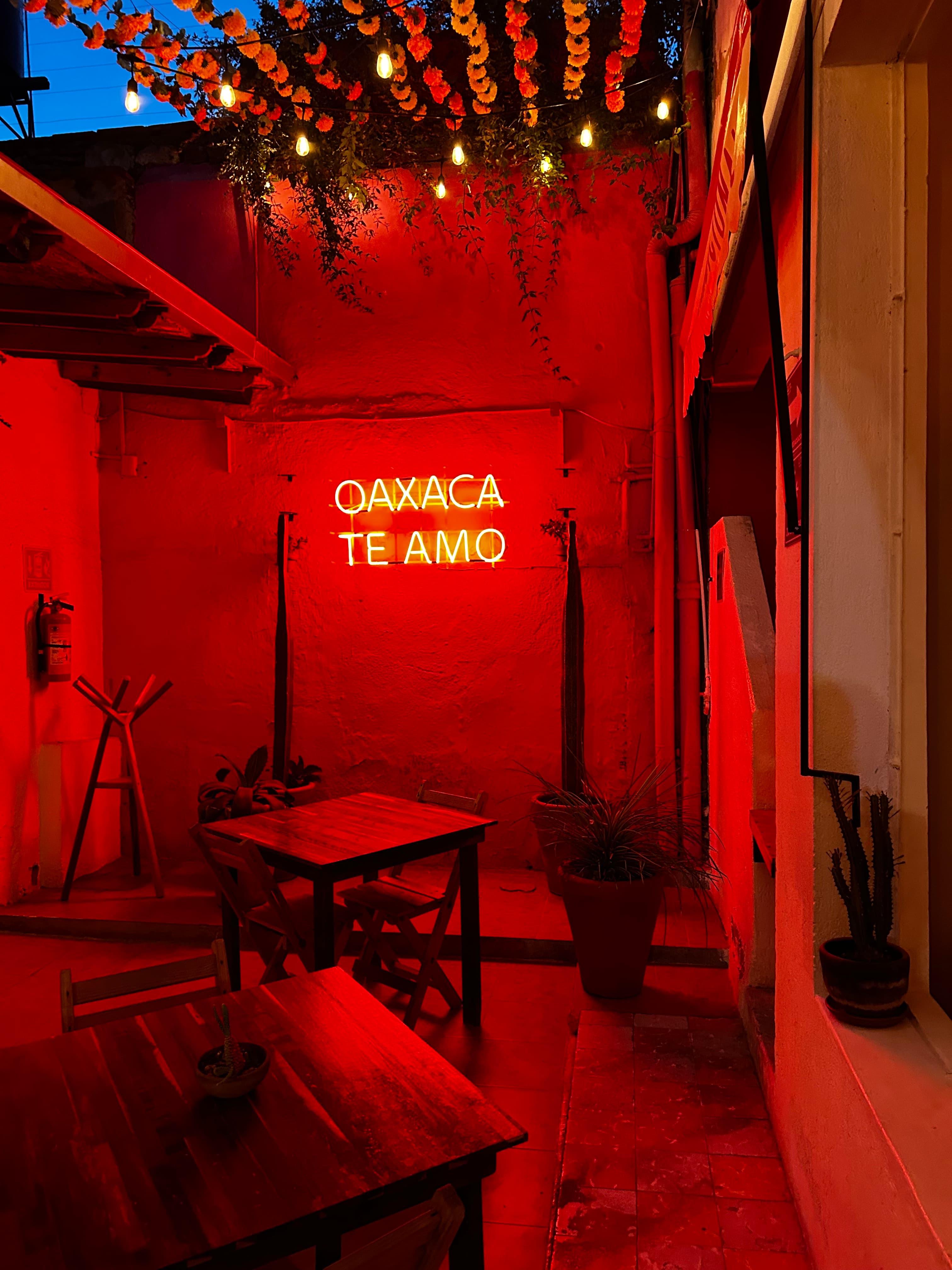 View of an indoor area with tables lit up red by a sign reading “OAXACA TE AMO”