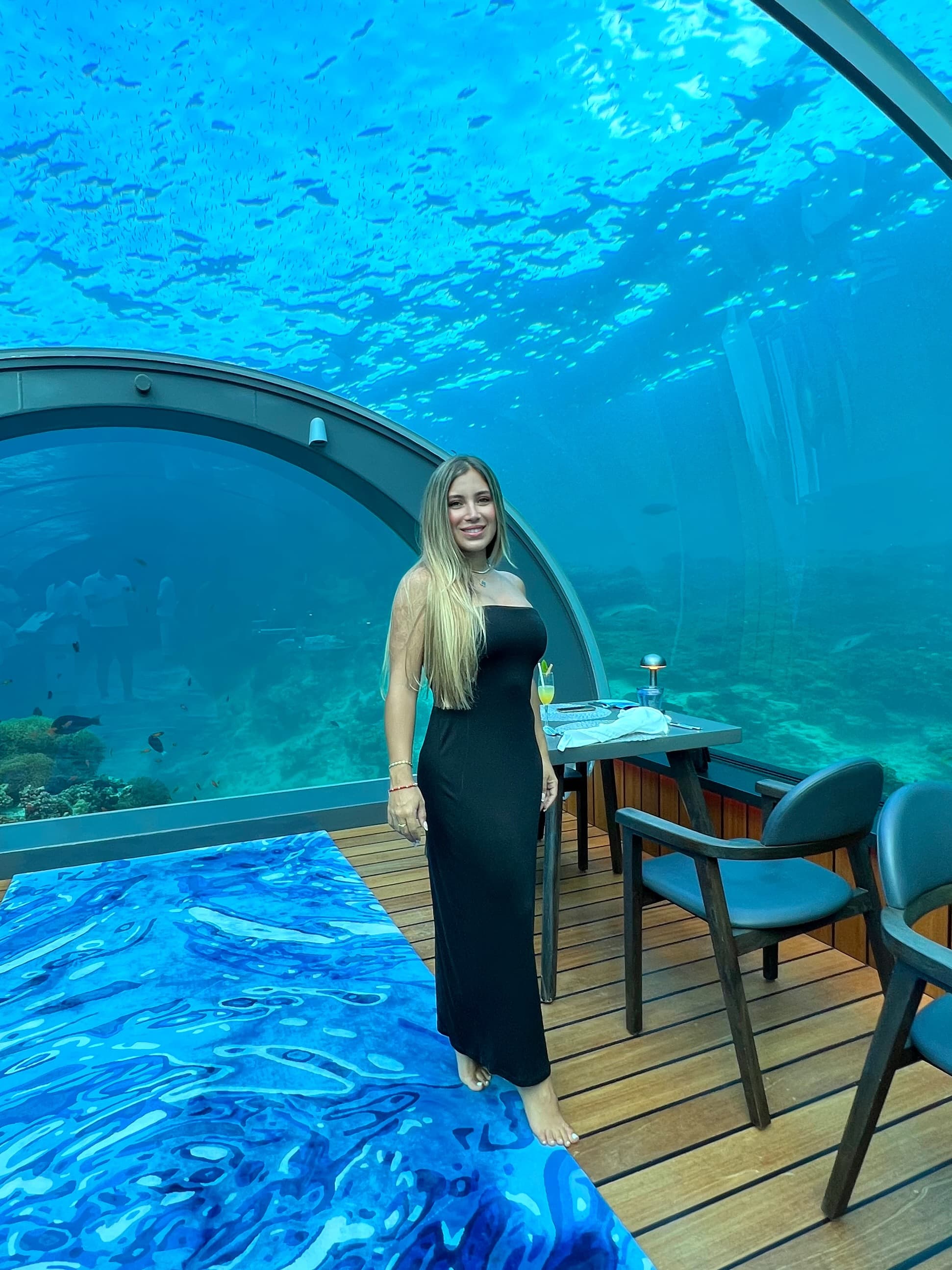 Advisor posing in an underwater restaurant with table settings and a glass dome with the ocean surrounding.