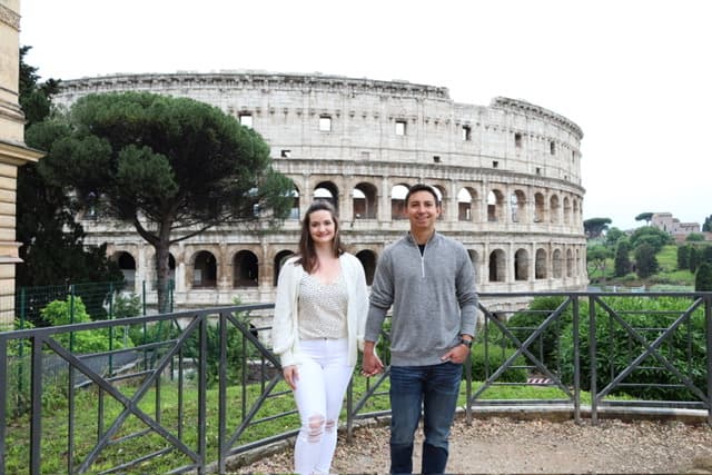 Jadyn and her partner hold hands with a full shot of the Colosseum behind them on a cloudy day