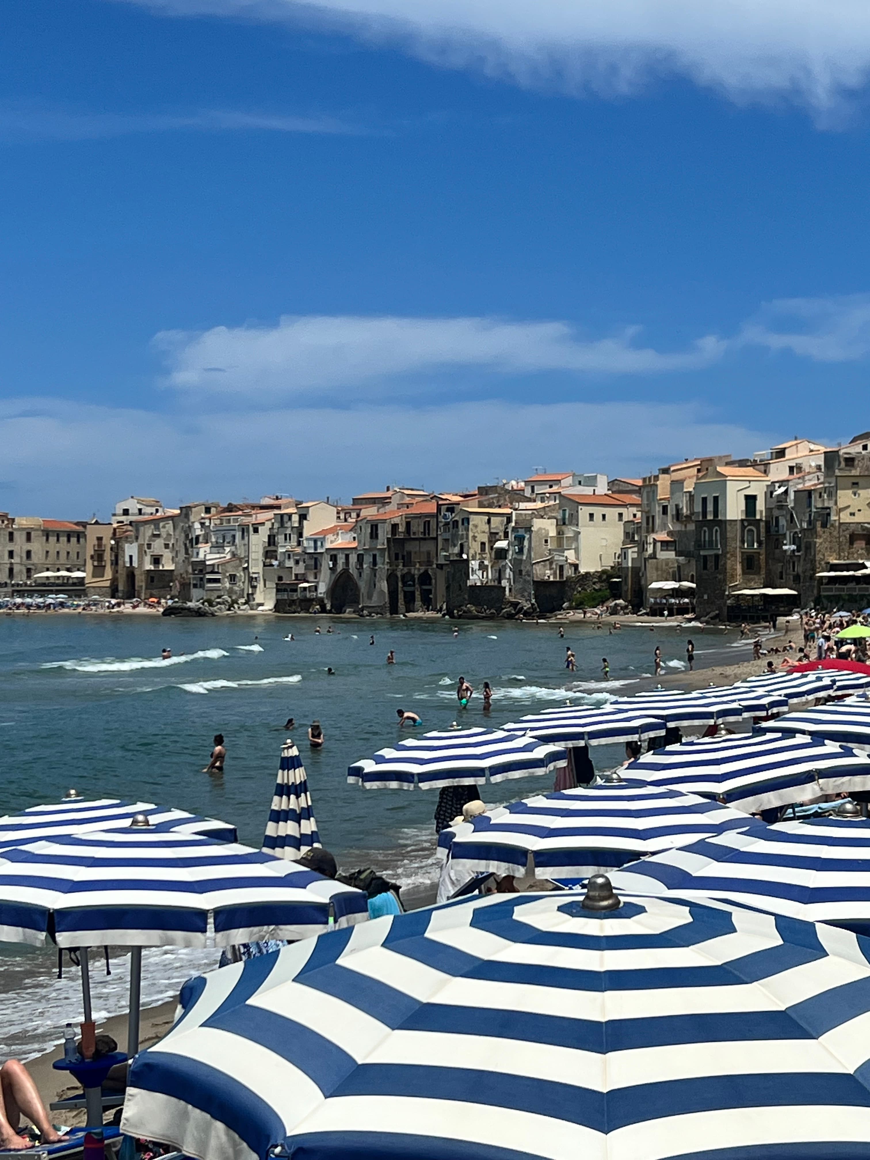 A view overlooking blue and white striped beach umbrellas, the ocean with tall white buildings along the coastline.