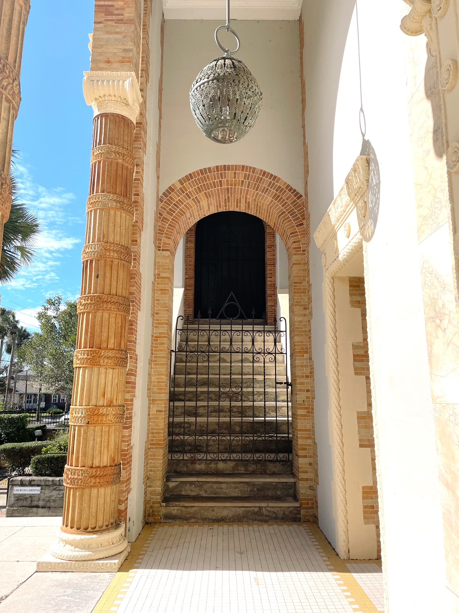 View of a stone doorway and gate with steps leading upwards into a dark area on a sunny day