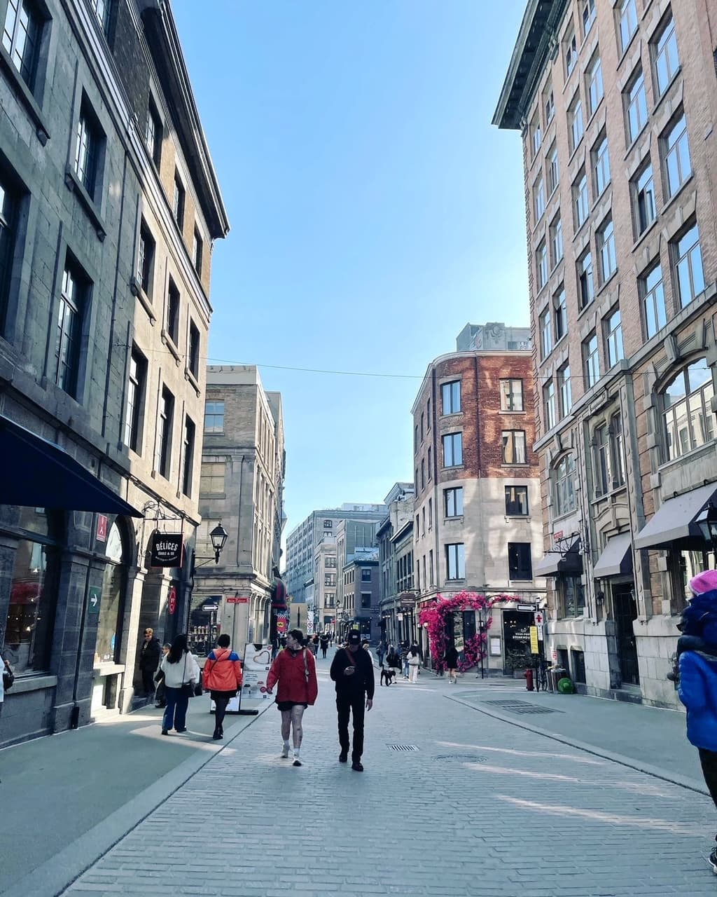 View of a wide city street lined with tall buildings and pedestrians walking on a clear day