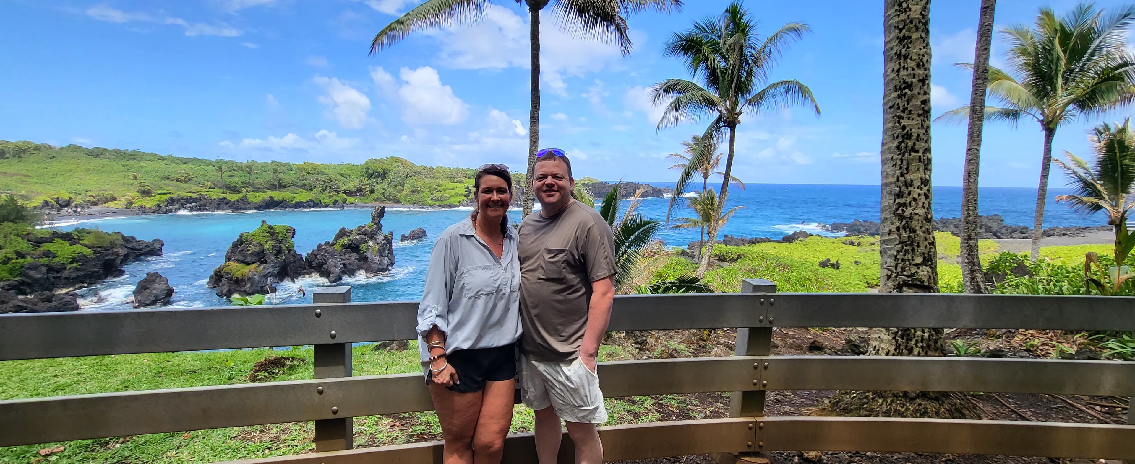 A couple standing with views of the sea and palm trees in the back.