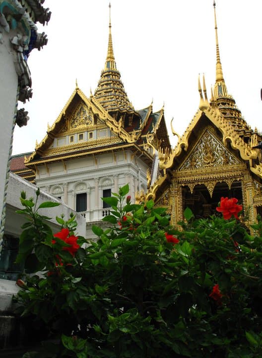 Pretty view of the golden spires atop a temple with green trees in front under cloudy skies