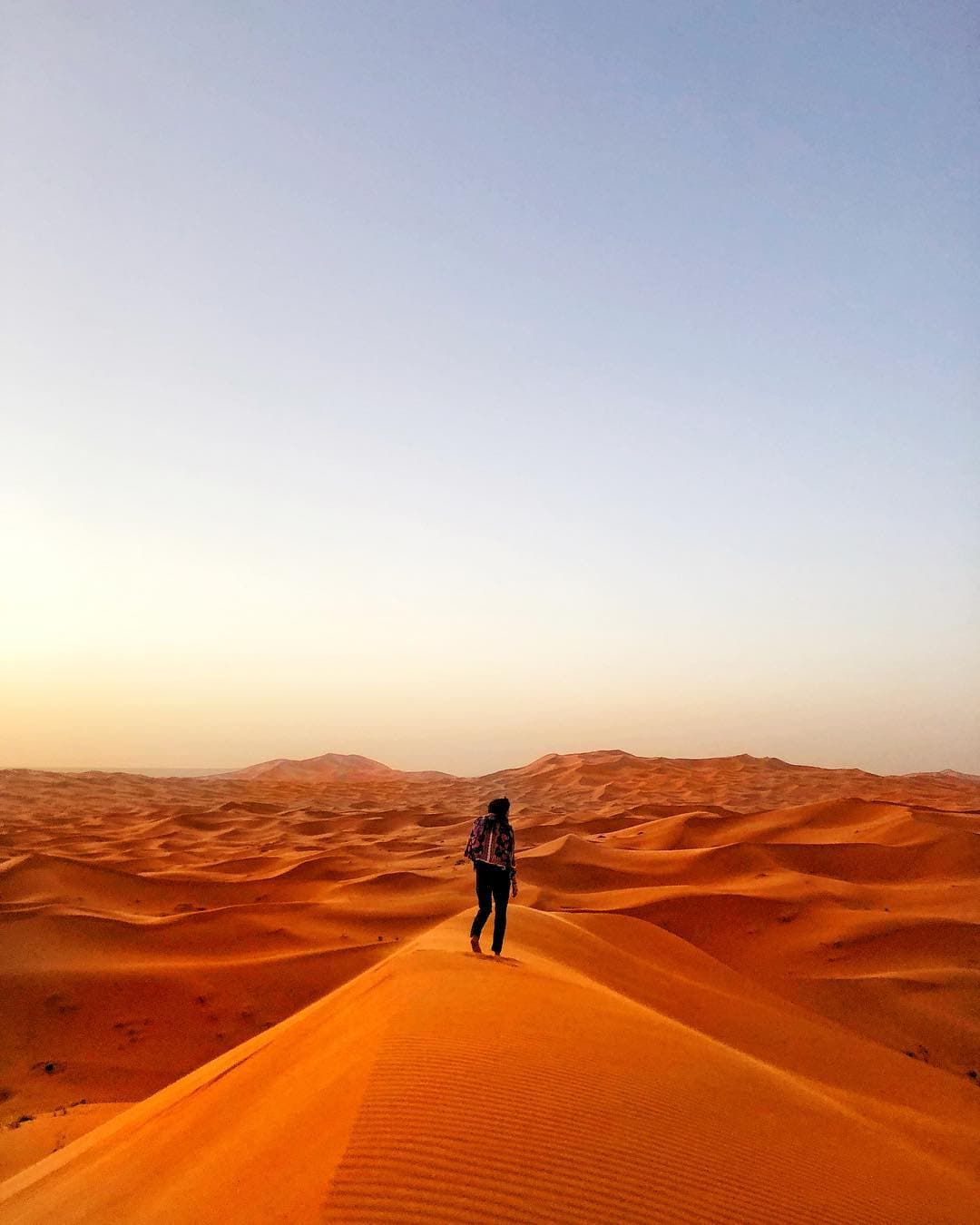 View of one person walking on an empty landscape of beautiful red sand dunes under clear skies