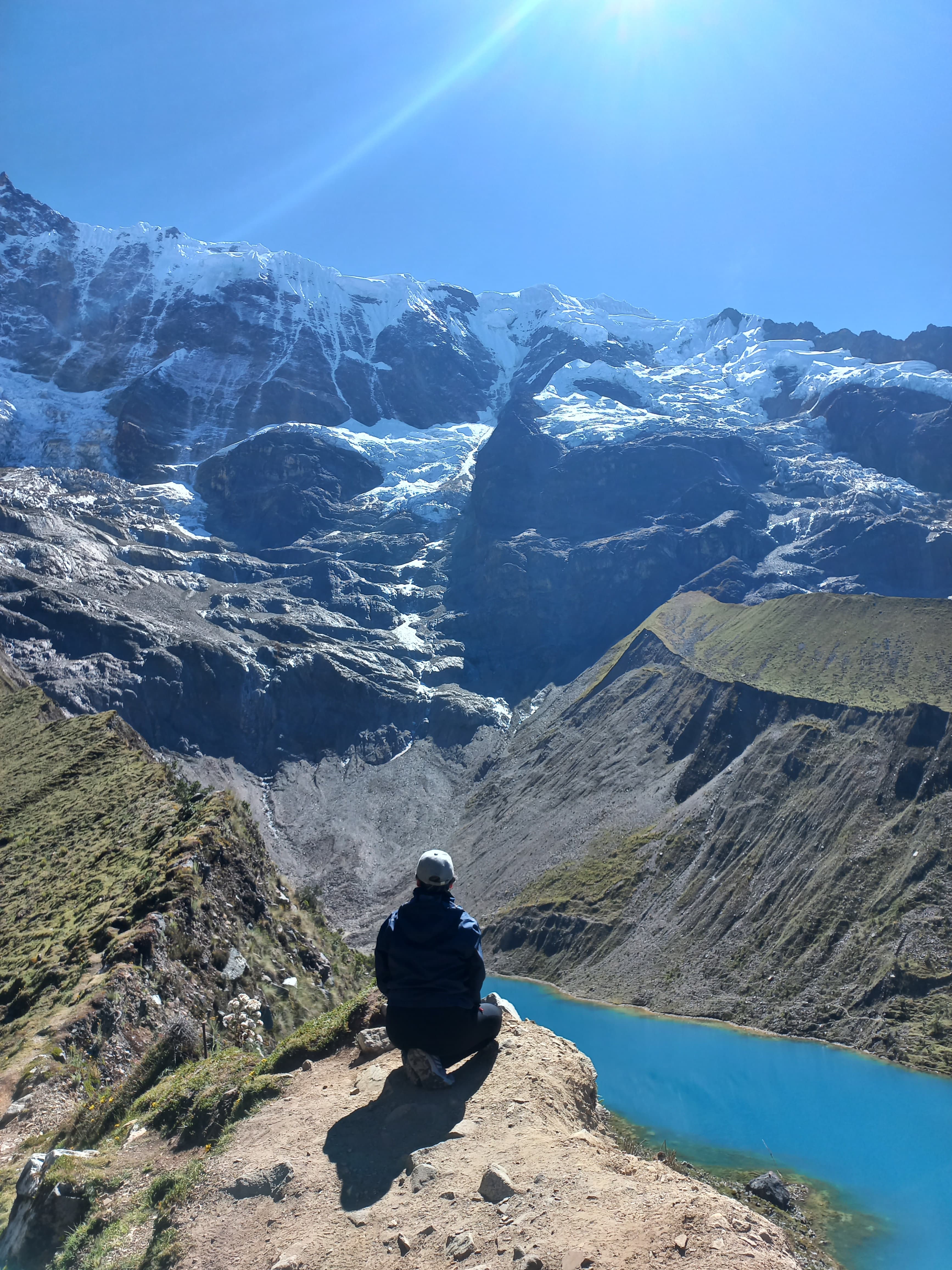 Rosa sitting on the edge of a cliff overlooking a gorgeous blue lake and snow-capped mountain view on a sunny day