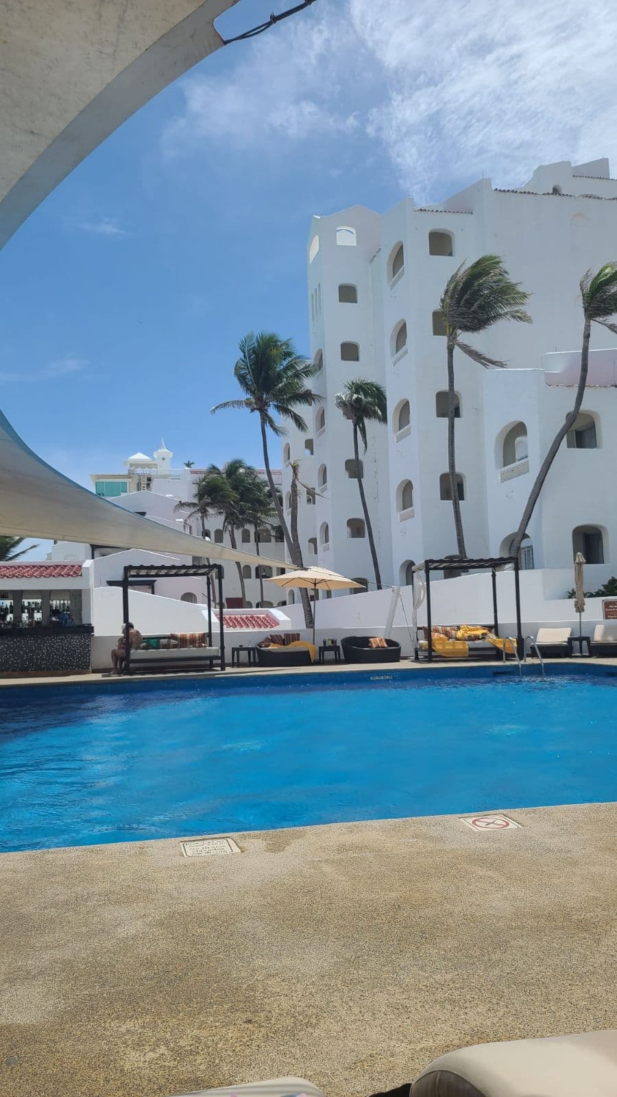 View of an empty resort pool surrounded by palm trees and a tall white building
