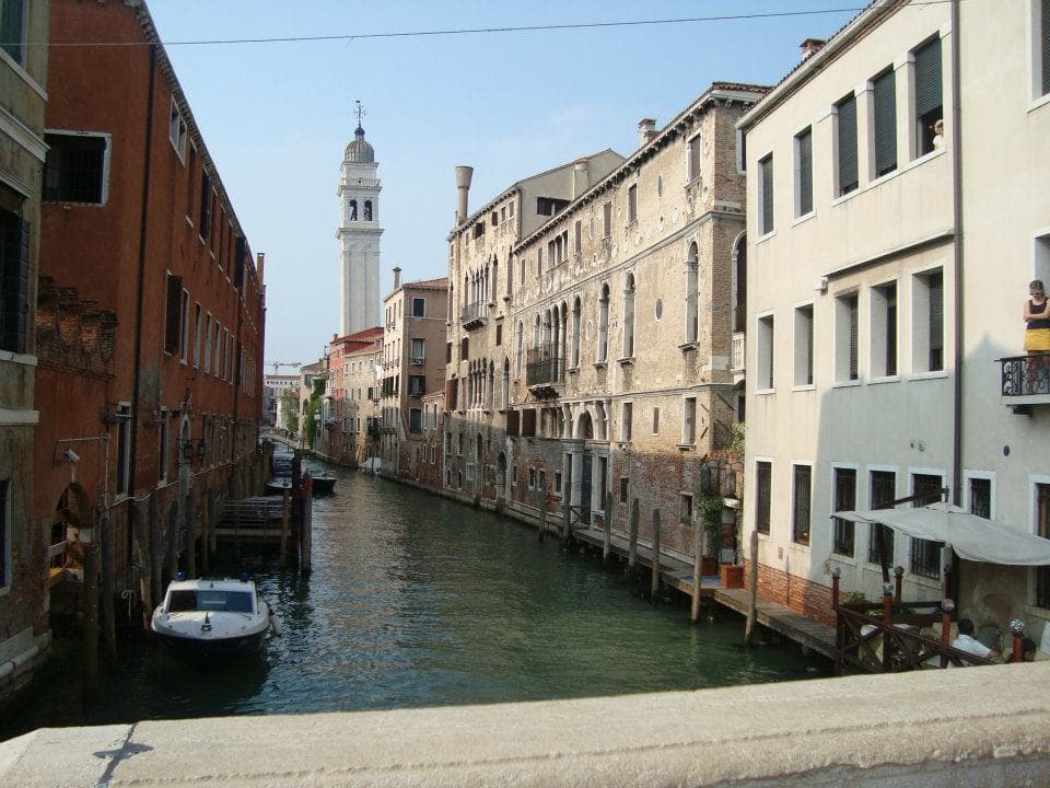 Pretty view of a canal lined with old buildings and small boats with a church tower visible in the distance under sunny skies