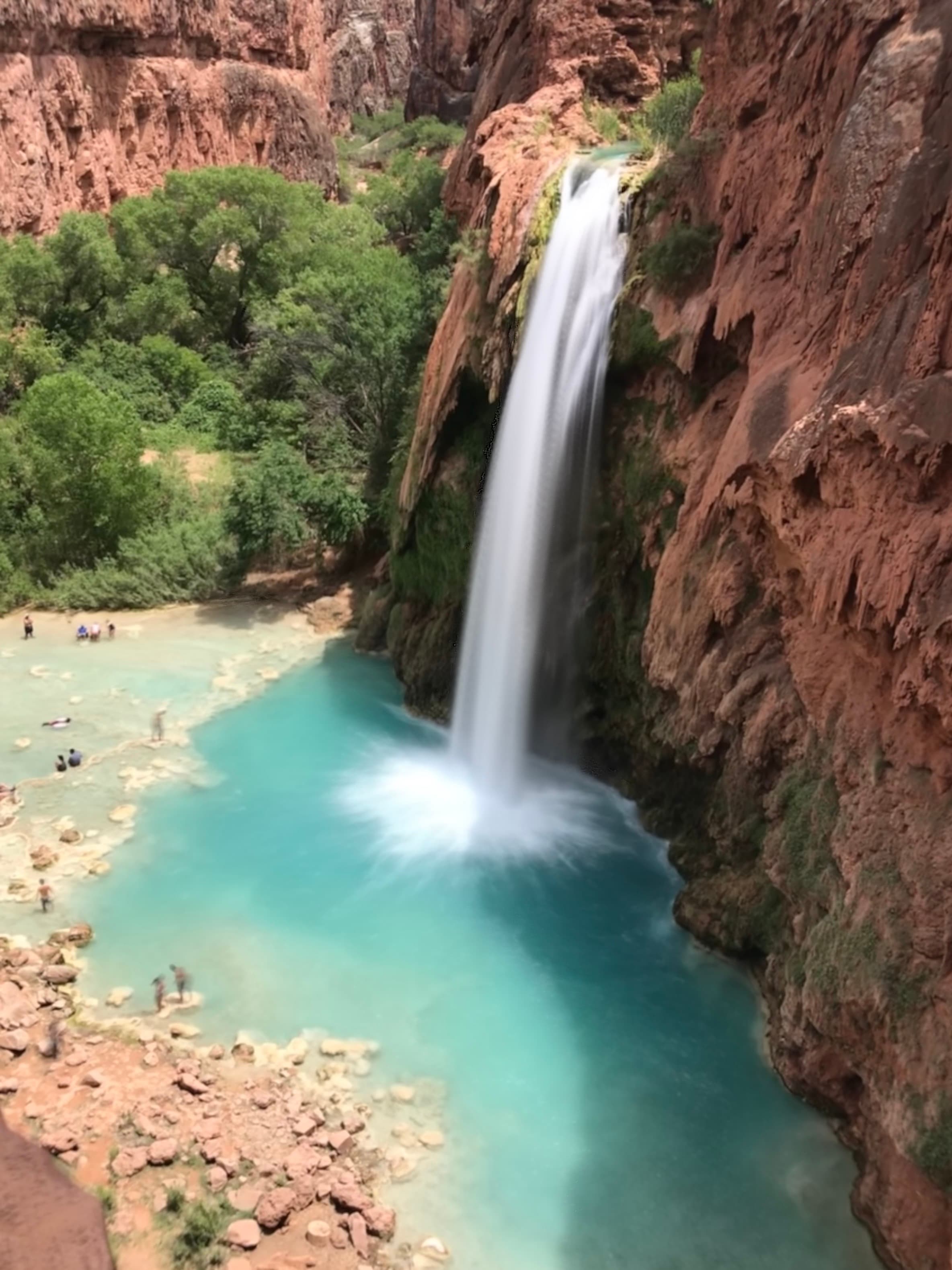 View of a beautiful waterfall pouring into a light blue body of water from a cliffside of red rocks