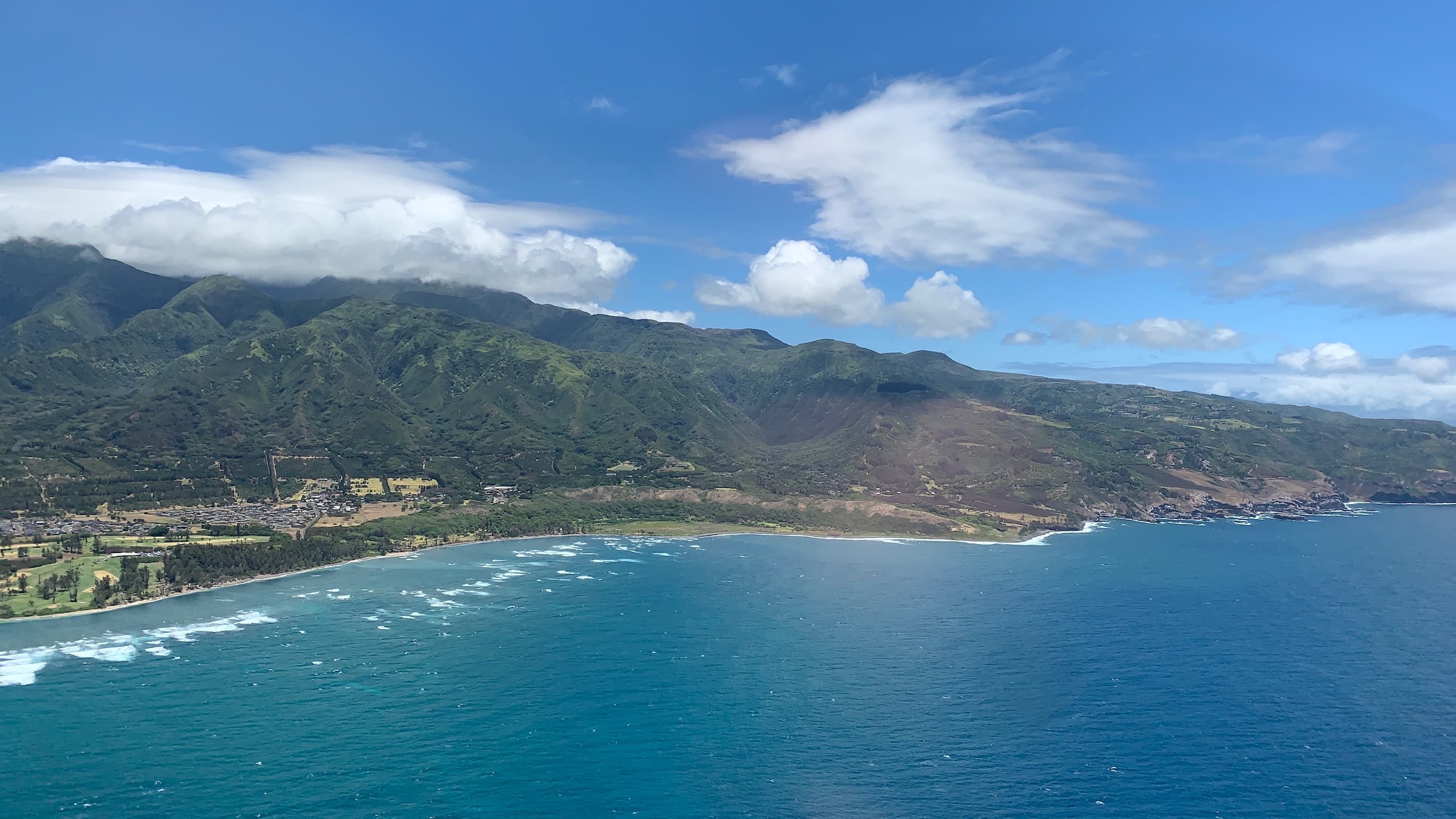 Beautiful aerial view of a coastline with green hills under sunny skies