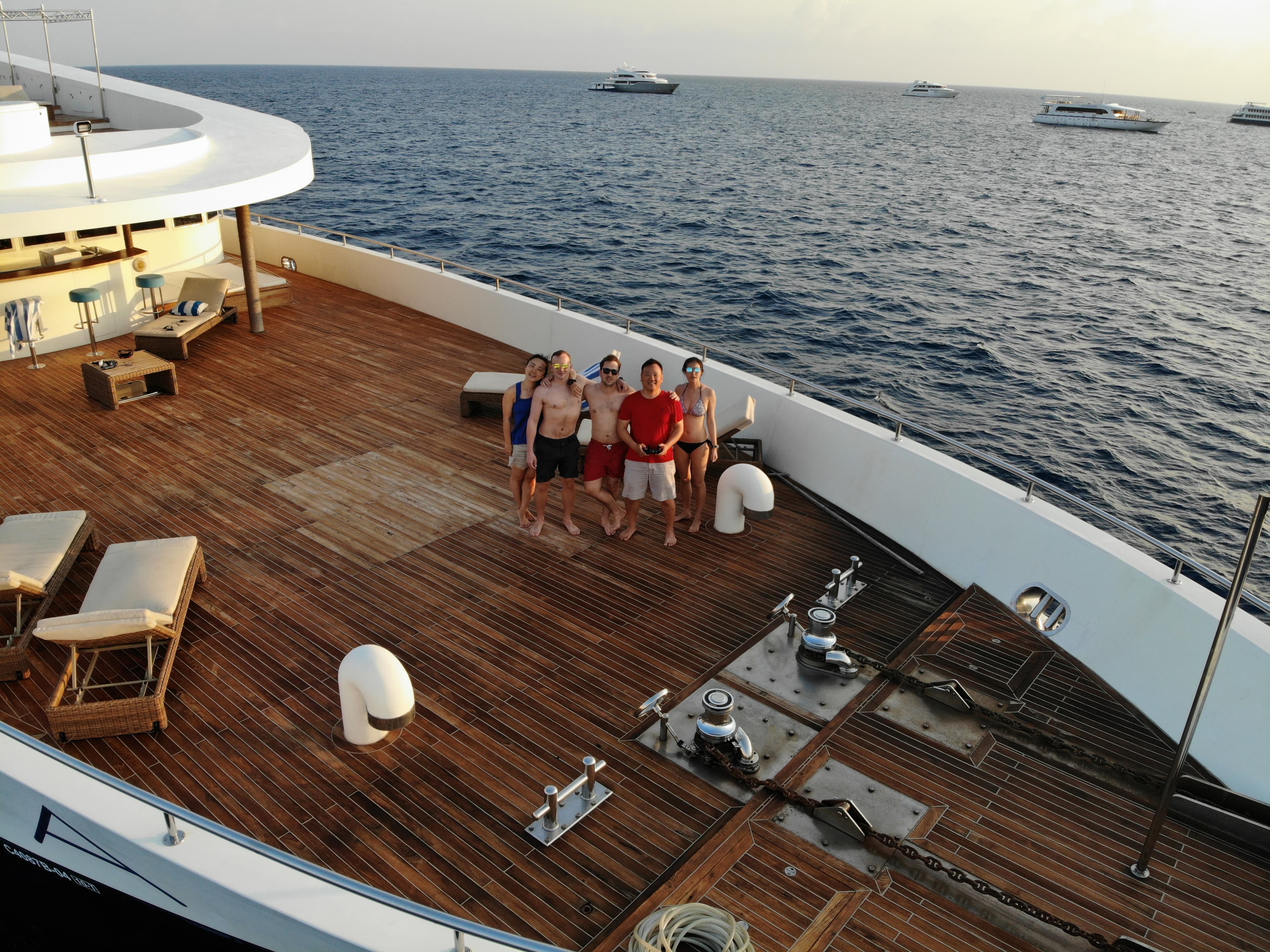 Aerial view of the wooden front deck of a large boat at sea with a group of people posing for a photo