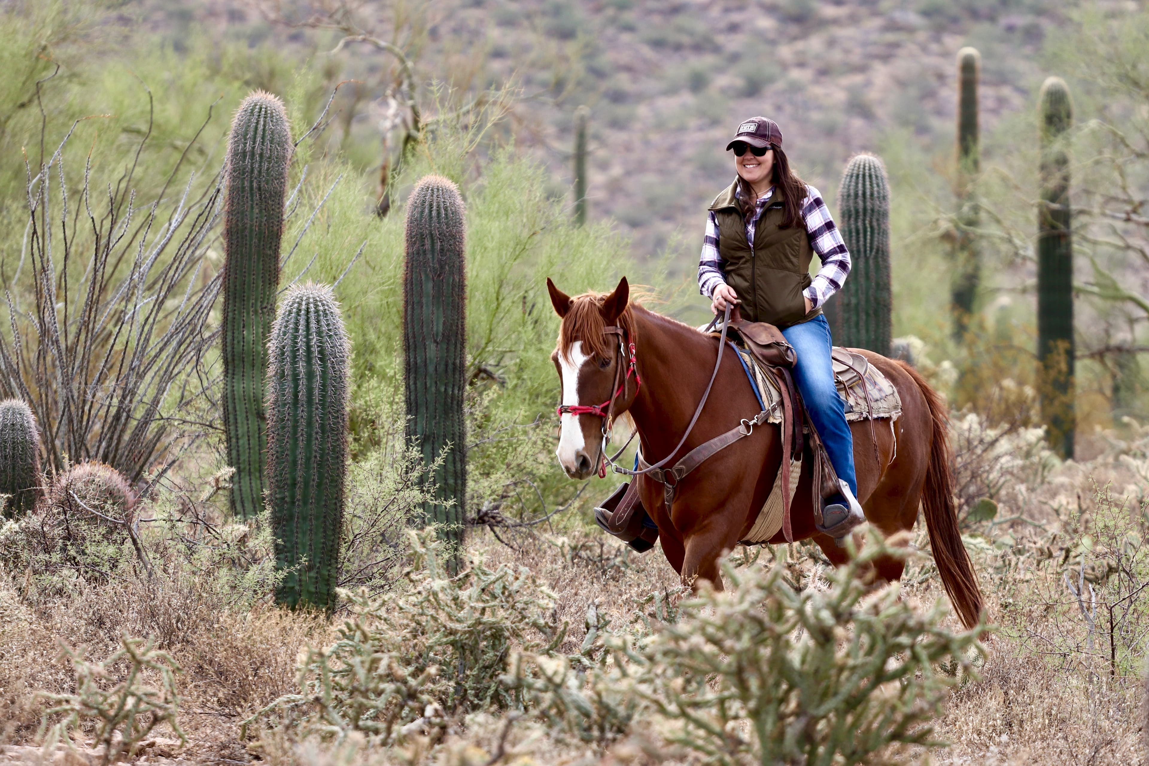 Dani in a striped shirt and vest on horseback among cacti