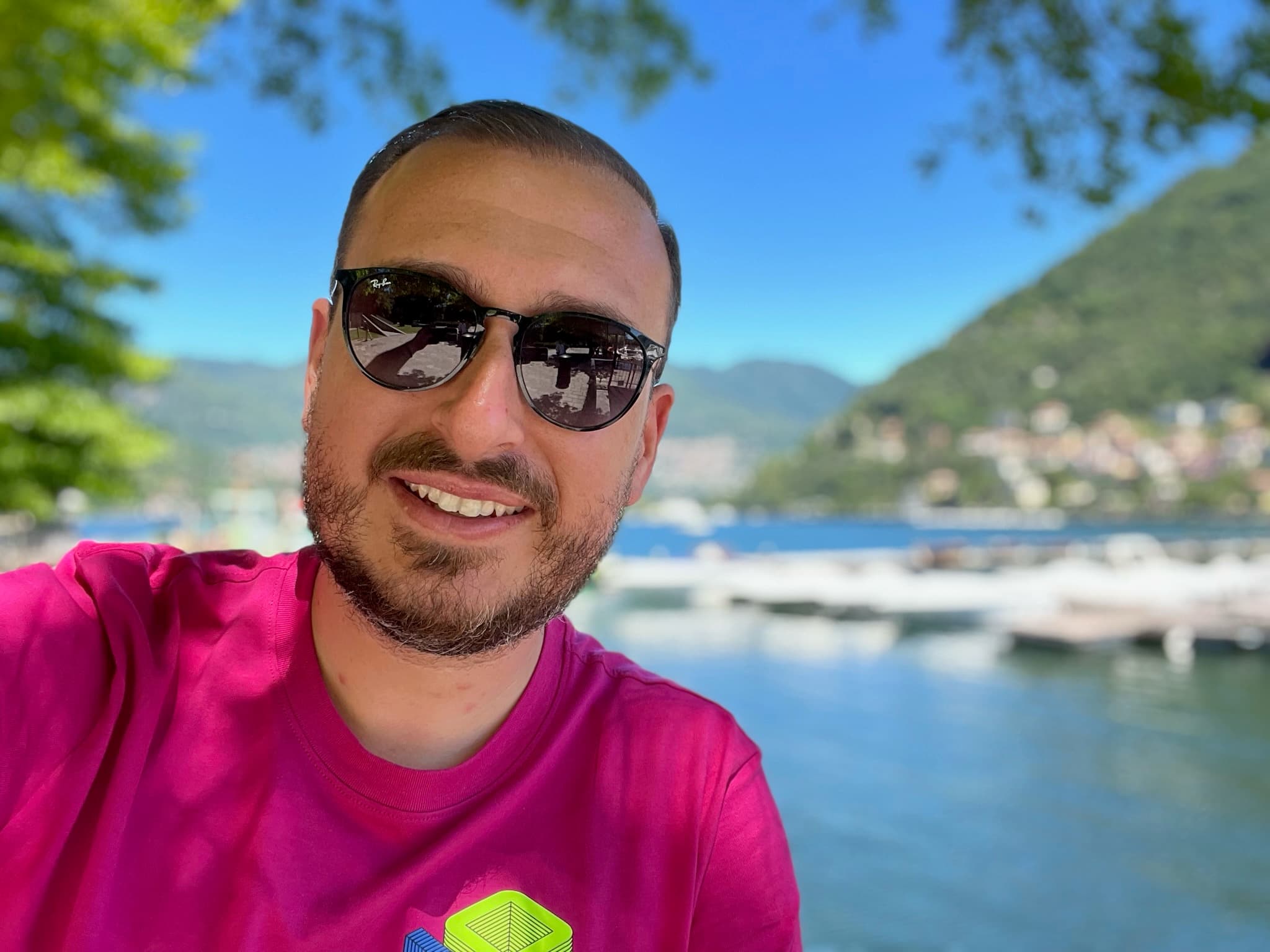 Photo of advisor posing with sunglasses and a pink shirt in front of a body of water.