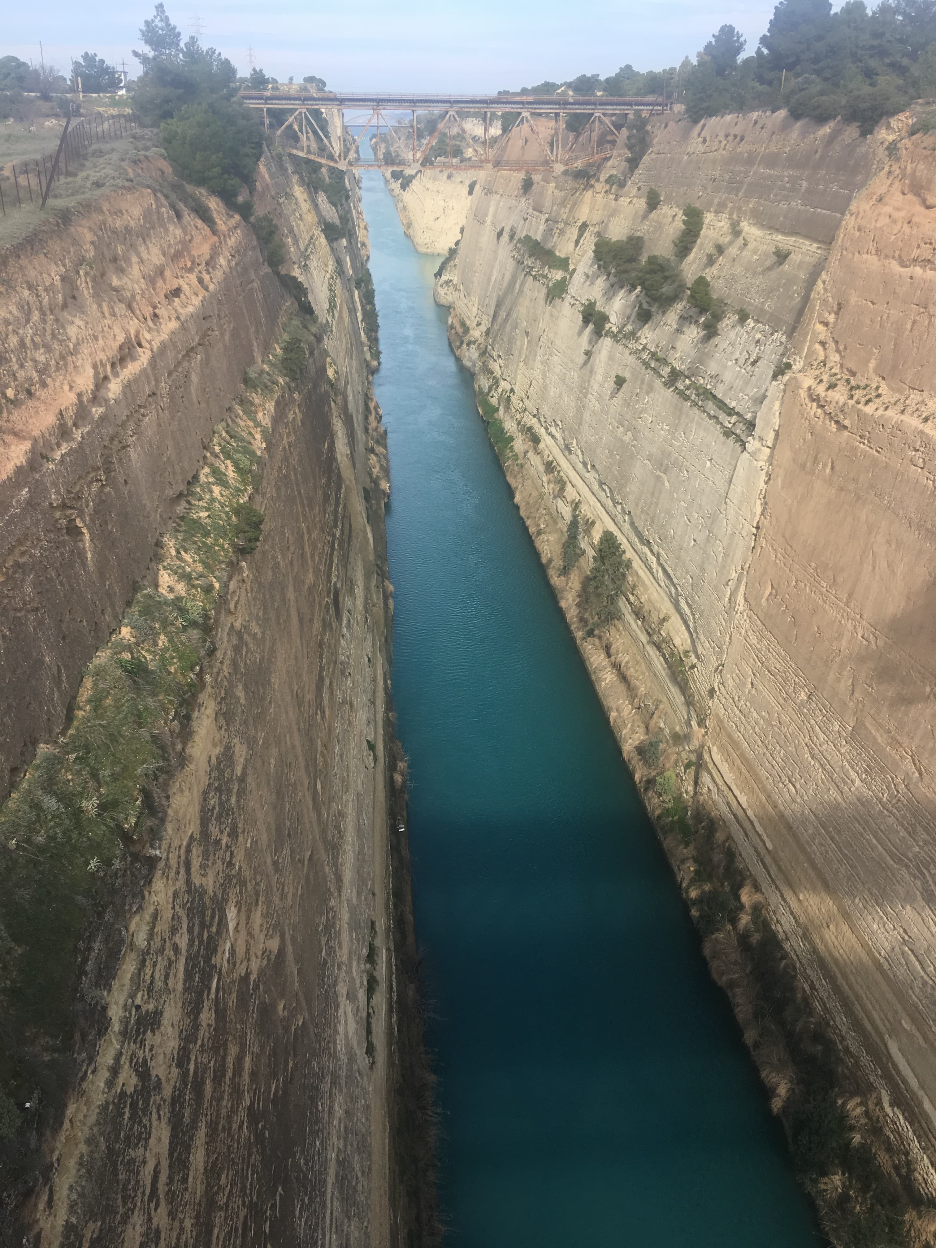 Narrow turquoise canal running between steep rock walls under a cloudy sky.