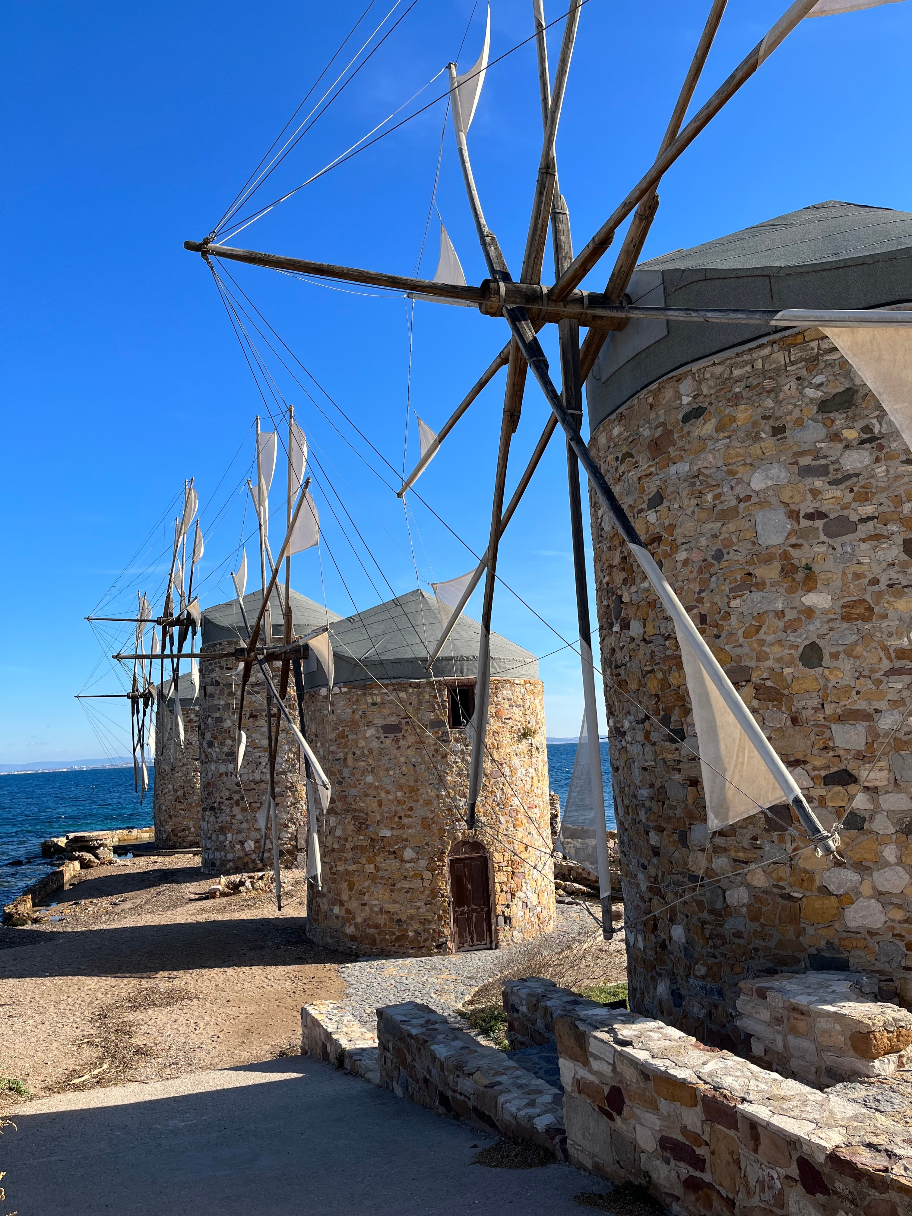 Historic stone windmills with wooden sails by the seaside on a clear, sunny day.