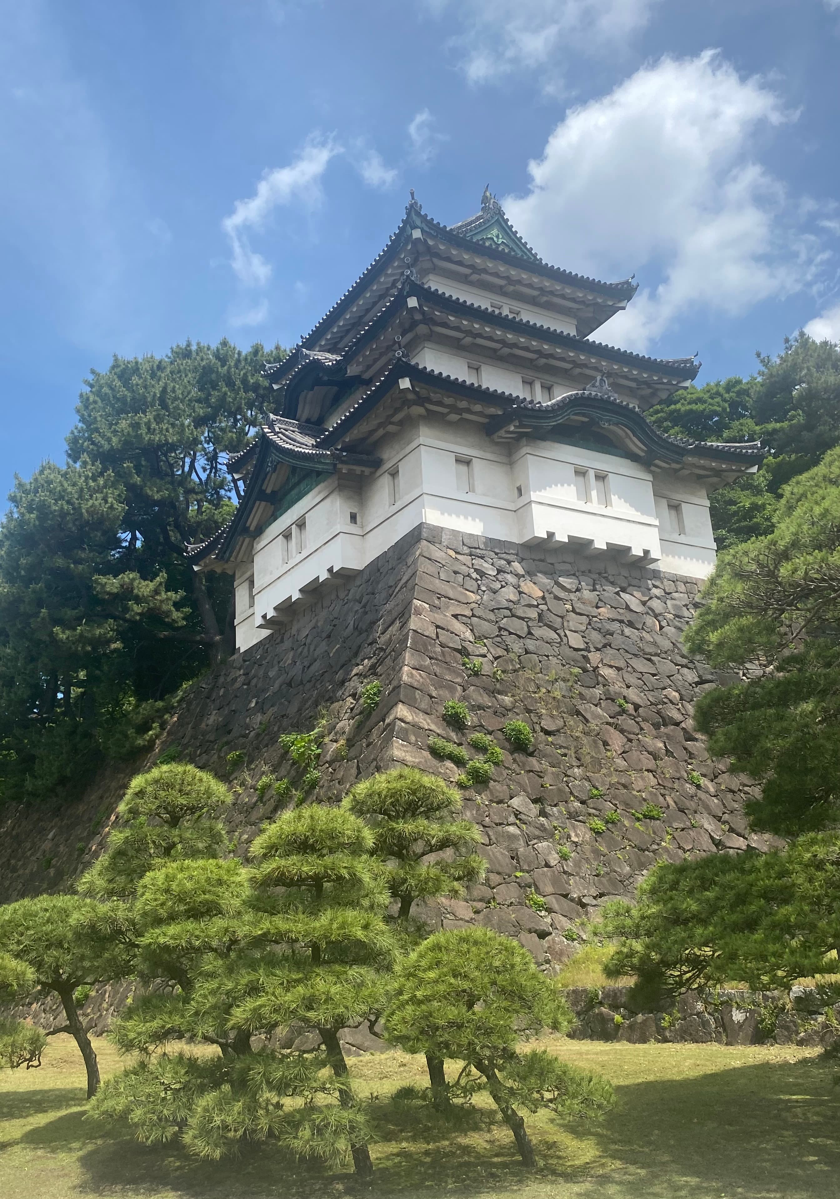 View of a white building atop a stone structure surrounded by trees under sunny skies