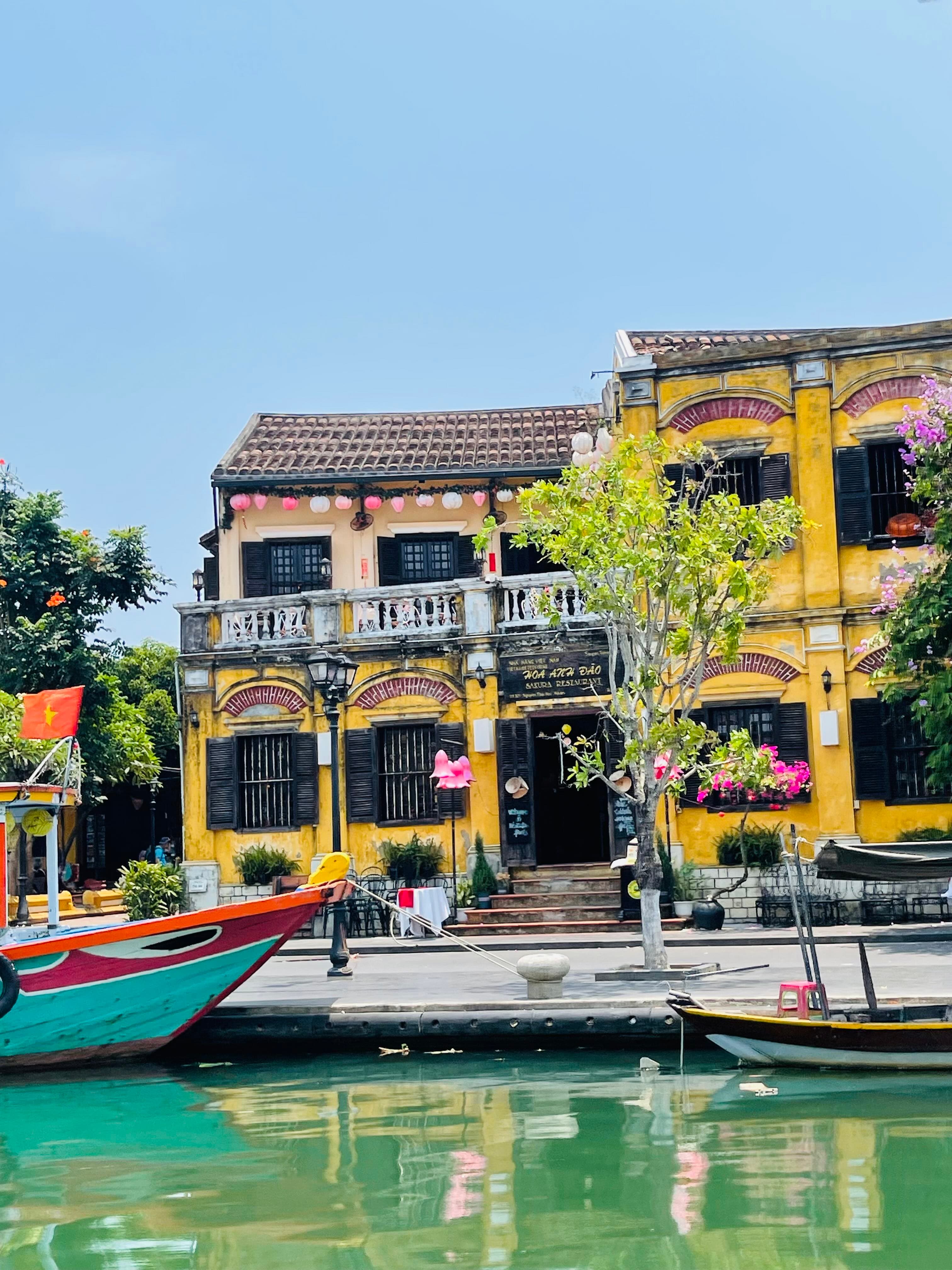 View of a beautiful yellow building along a canal with small boats visible docked to one side on a sunny day