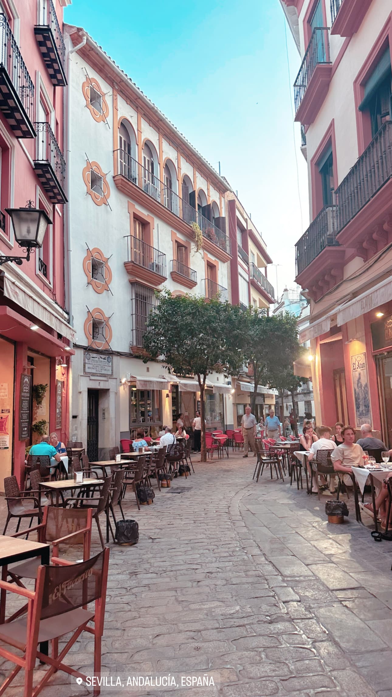A view of a stone street with buildings on both sides and people dining at restuarants on either side.